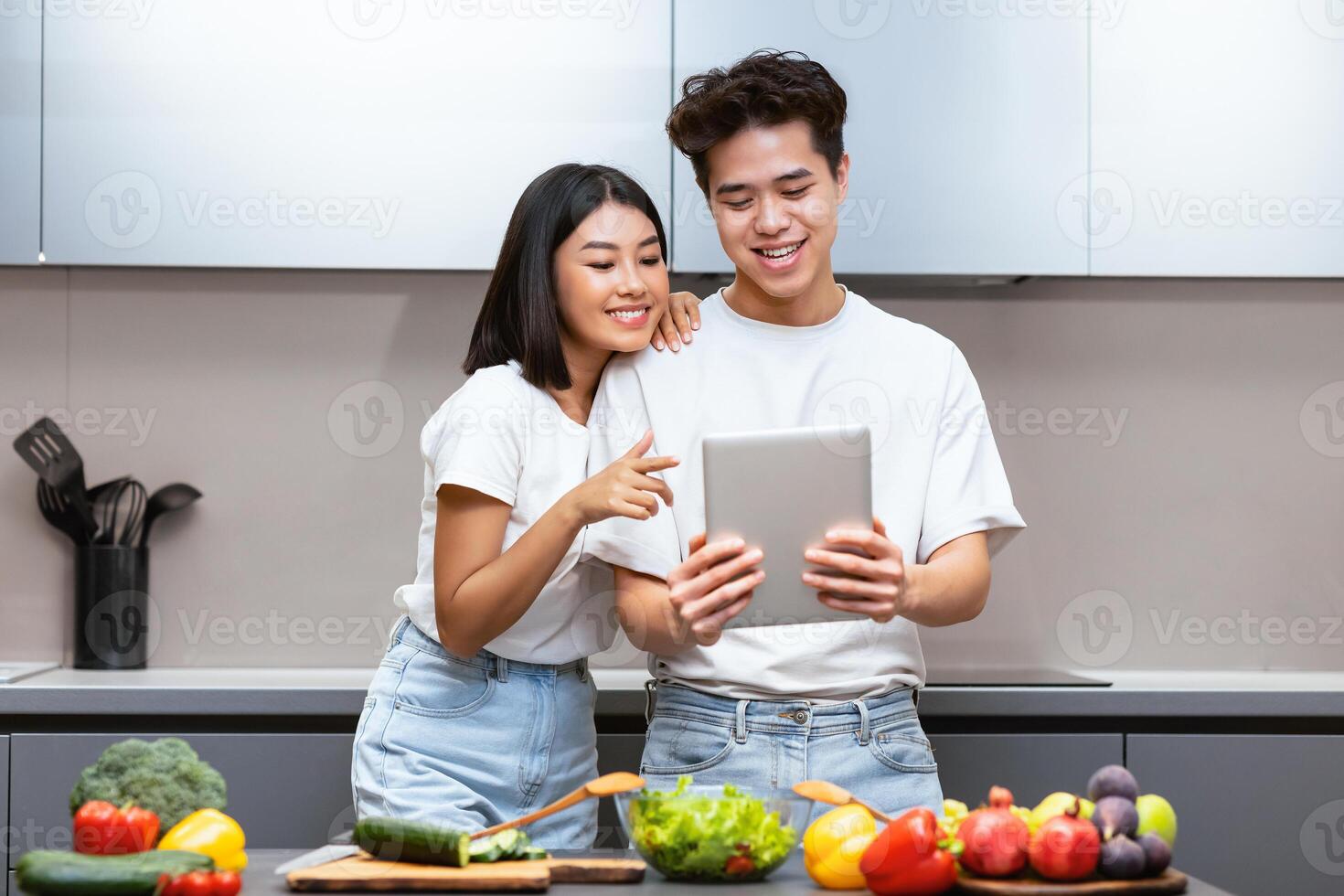 Asian Family Couple Cooking Using Digital Tablet Searching Recipe Online For Dinner Standing In Kitchen At Home. Best Food Recipes App, Cook Meal Applications Concept photo