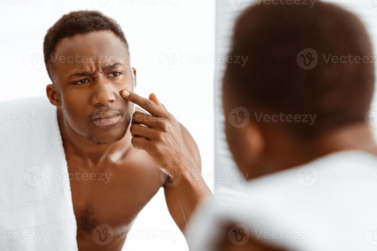 Problem Skin. Sad African American Man Touching Acne Pimple On Face Looking At His Reflection In Mirror Standing In Modern Bathroom At Home. Dermatology, Male Facial Skincare Concept. Selective Focus photo