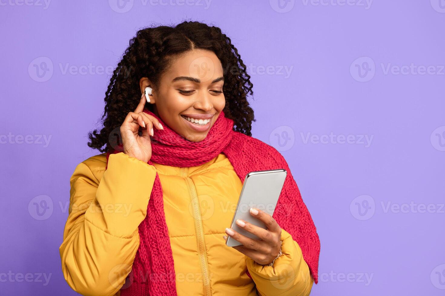 Black Woman With Mobile Phone And Earbuds Making Call Or Listening To Music Online In Earphones Standing Over Blue Studio Background. Gadget, Distant Communication Concept. Free Space photo