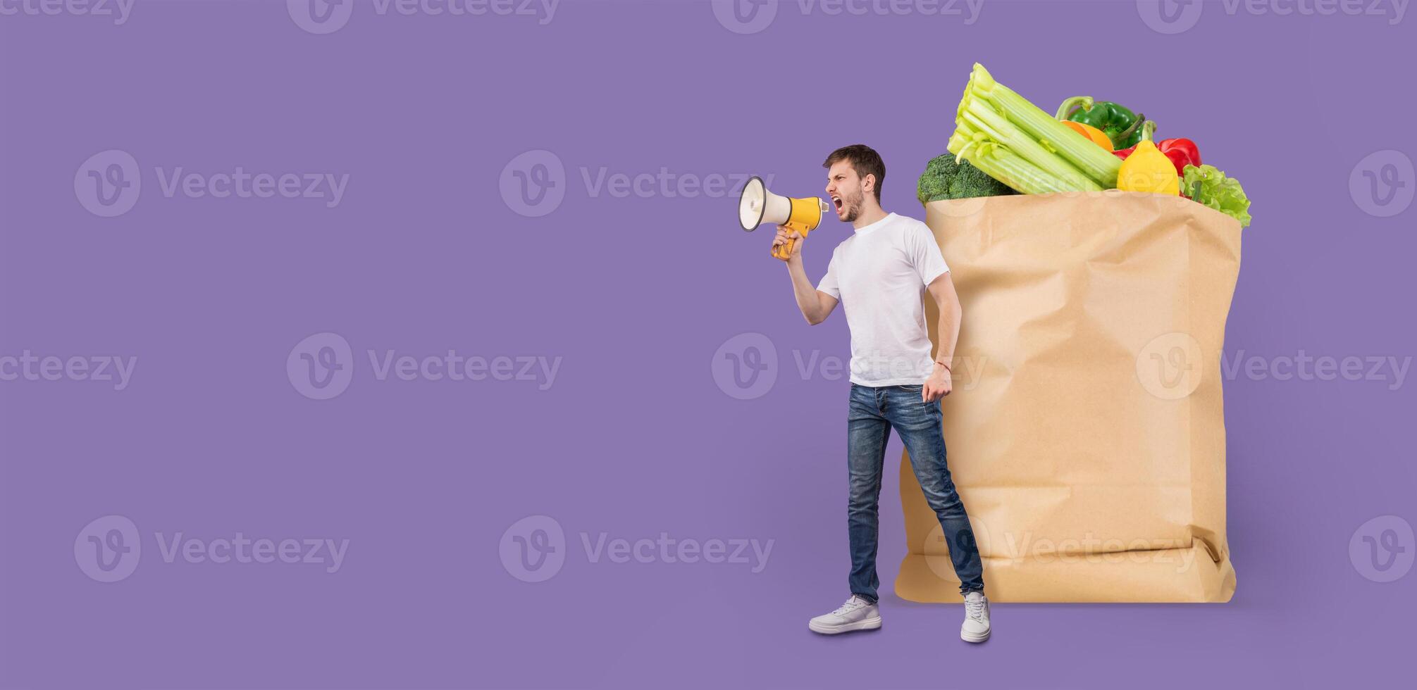 A customer stands beside a large paper grocery bag filled with fresh produce. He is holding a megaphone and appears to be making an announcement about shopping. photo