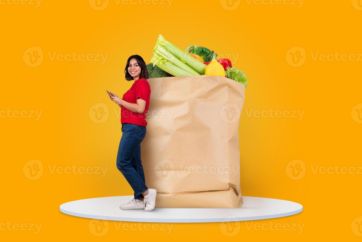 A customer stands beside a large paper bag overflowing with fresh vegetables and fruits, while checking their smartphone. This represents modern shopping habits and remote delivery options. photo