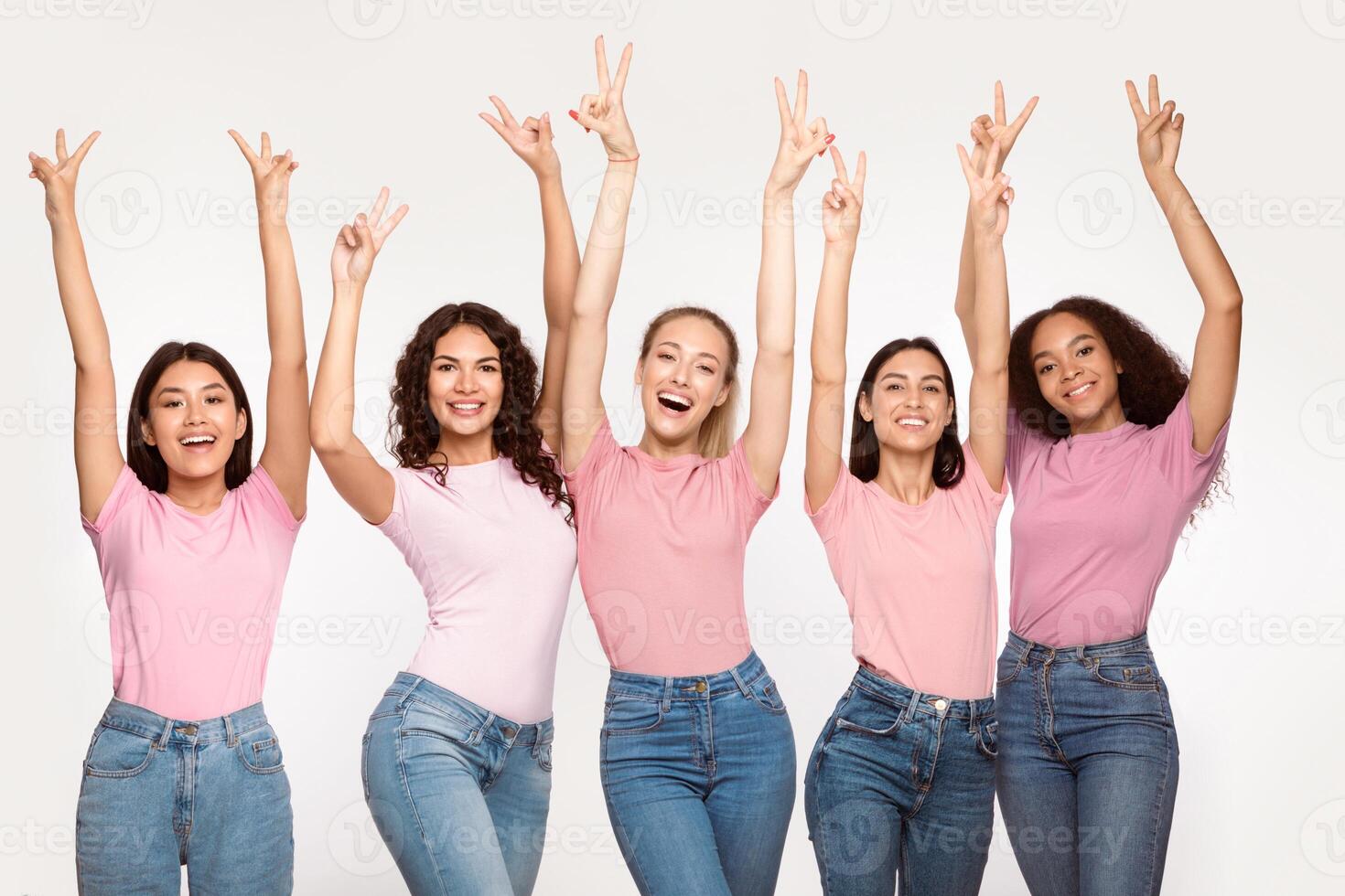 Group Of Positive Young Ladies Gesturing V-Sign Raising Hands Posing Standing Over White Studio Background, Smiling To Camera. Winners, Victory Celebration, Gestures And Emotions Concept photo