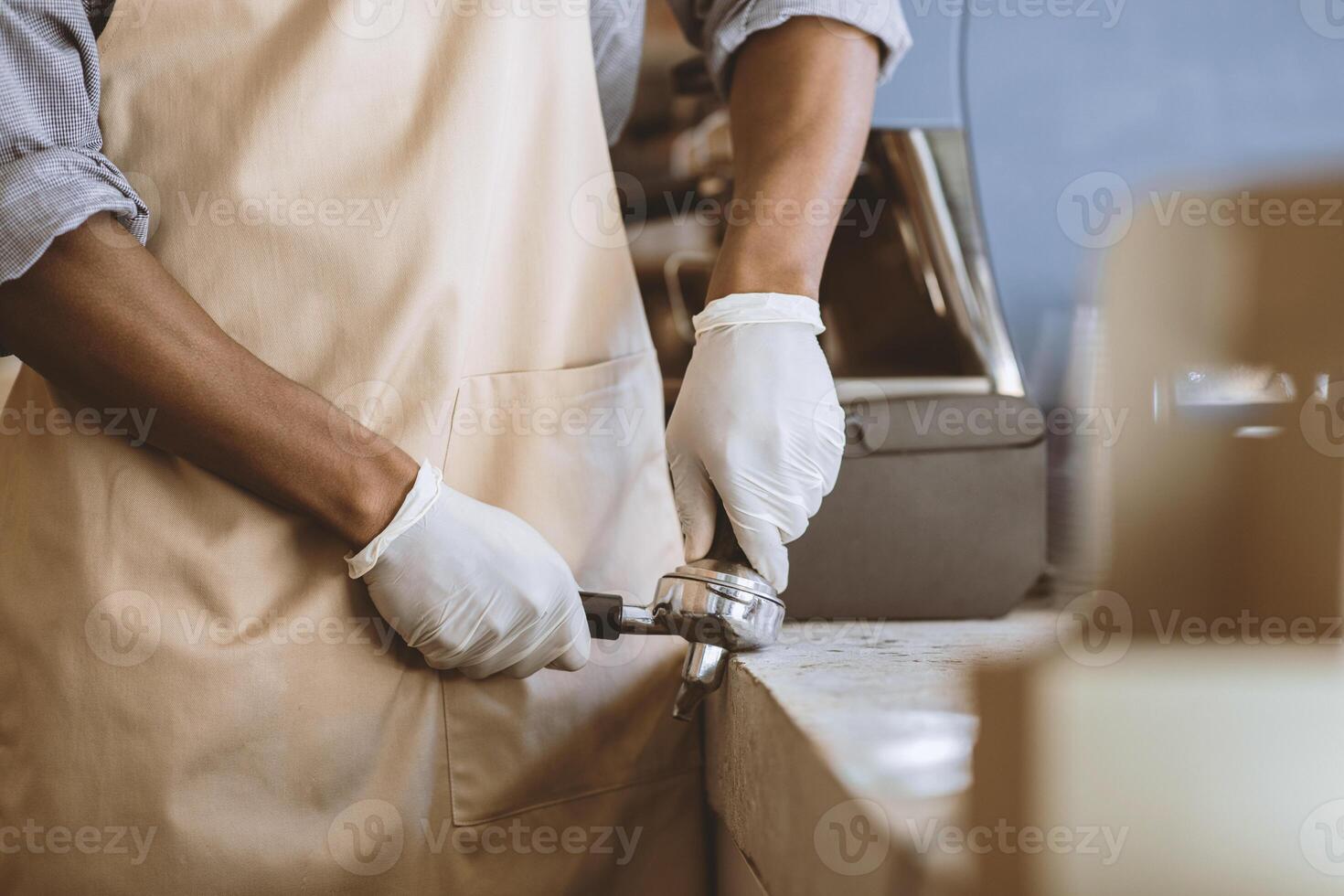 Takeaway coffee in modern cafeteria and new normal. Millennial african american guy in white gloves and apron works with equipment for making espresso in coffee shop during covid-19 pandemic, cropped photo