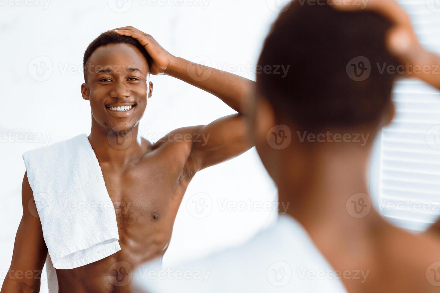 Shirtless African American Man Touching Hair Looking In Mirror After Shower Smiling To His Reflection Standing In Modern Bathroom At Home. Male Beauty And Haircare Routine. Selective Focus photo