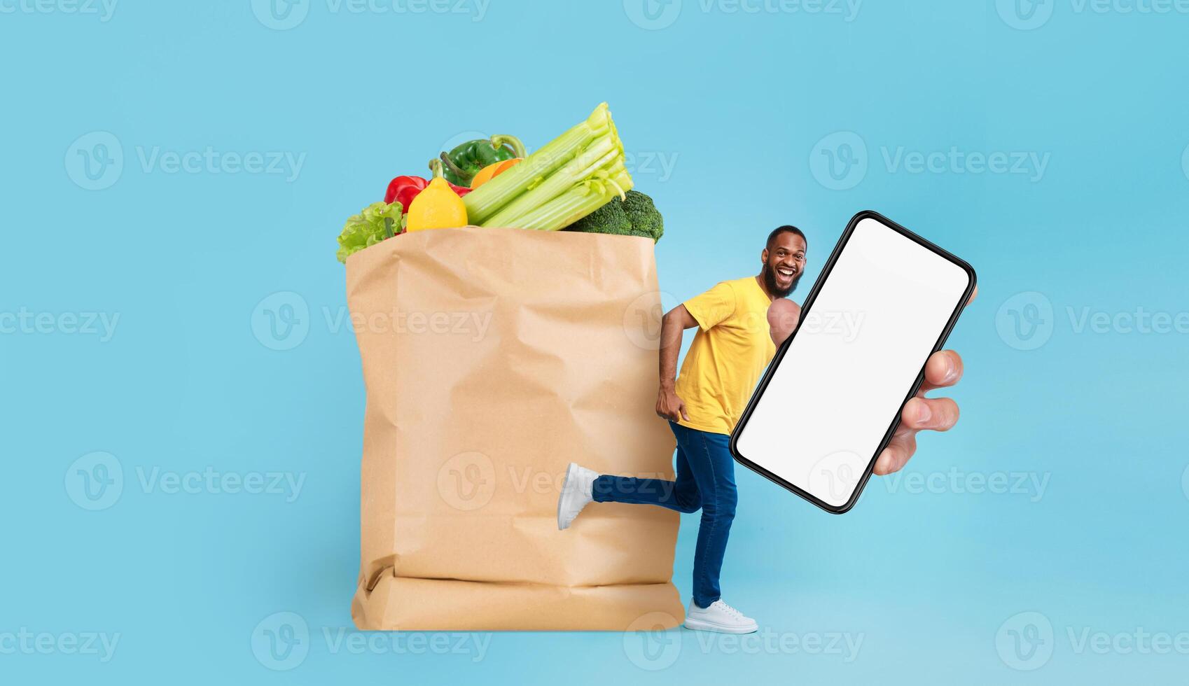 A customer holding a smartphone runs alongside a large paper bag filled with fresh groceries. The bright blue background emphasizes the convenience of shopping in today's new normal. photo