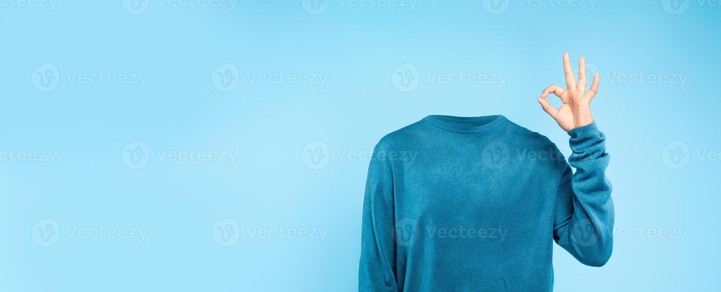 A headless individual dressed in a blue sweater makes a gesture of approval against a plain blue backdrop. This unique representation emphasizes a minimalist and surreal lifestyle concept. photo