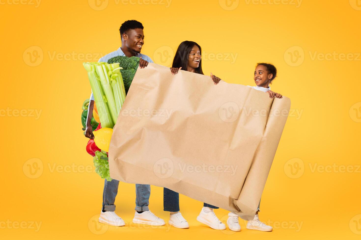 A cheerful family is carrying fresh vegetables, smiling and enjoying their grocery shopping experience. The vibrant yellow background highlights their joyful moment together. photo