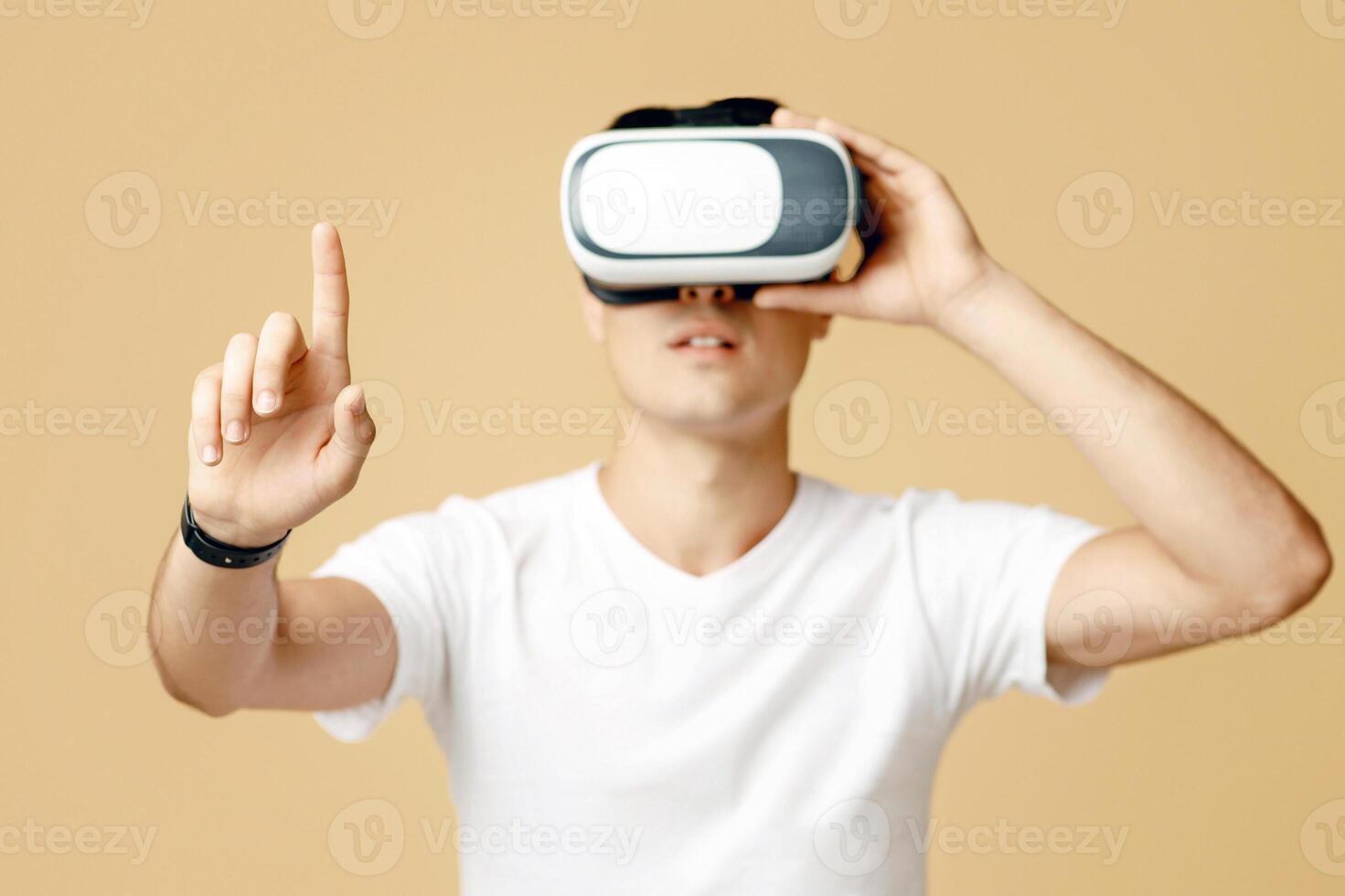 Man in vr glasses playing games with virtual reality headset trying to touch something with finger. Surprised young man student in white t-shirt use blank space, isolated on light background photo