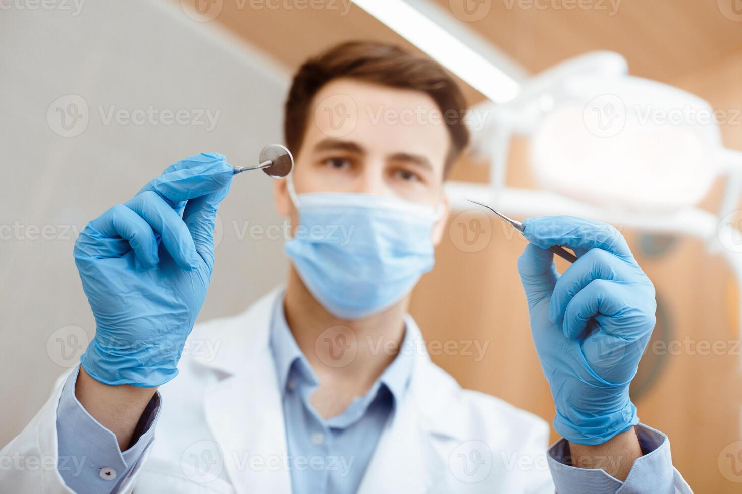 Dentist examining and teeth care. Millennial friendly stomatologist in white coat, protective mask and rubber gloves working with professional equipment in clinic office, bottom view, copy space photo