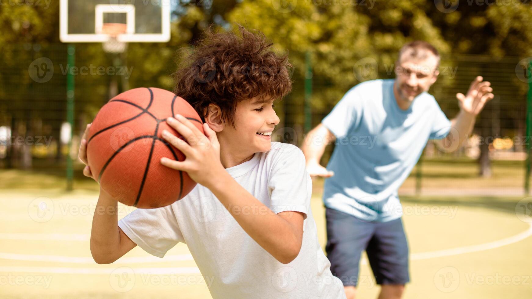 Having Fun. Son and dad playing basketball, joyful kid running from father holding ball, banner photo