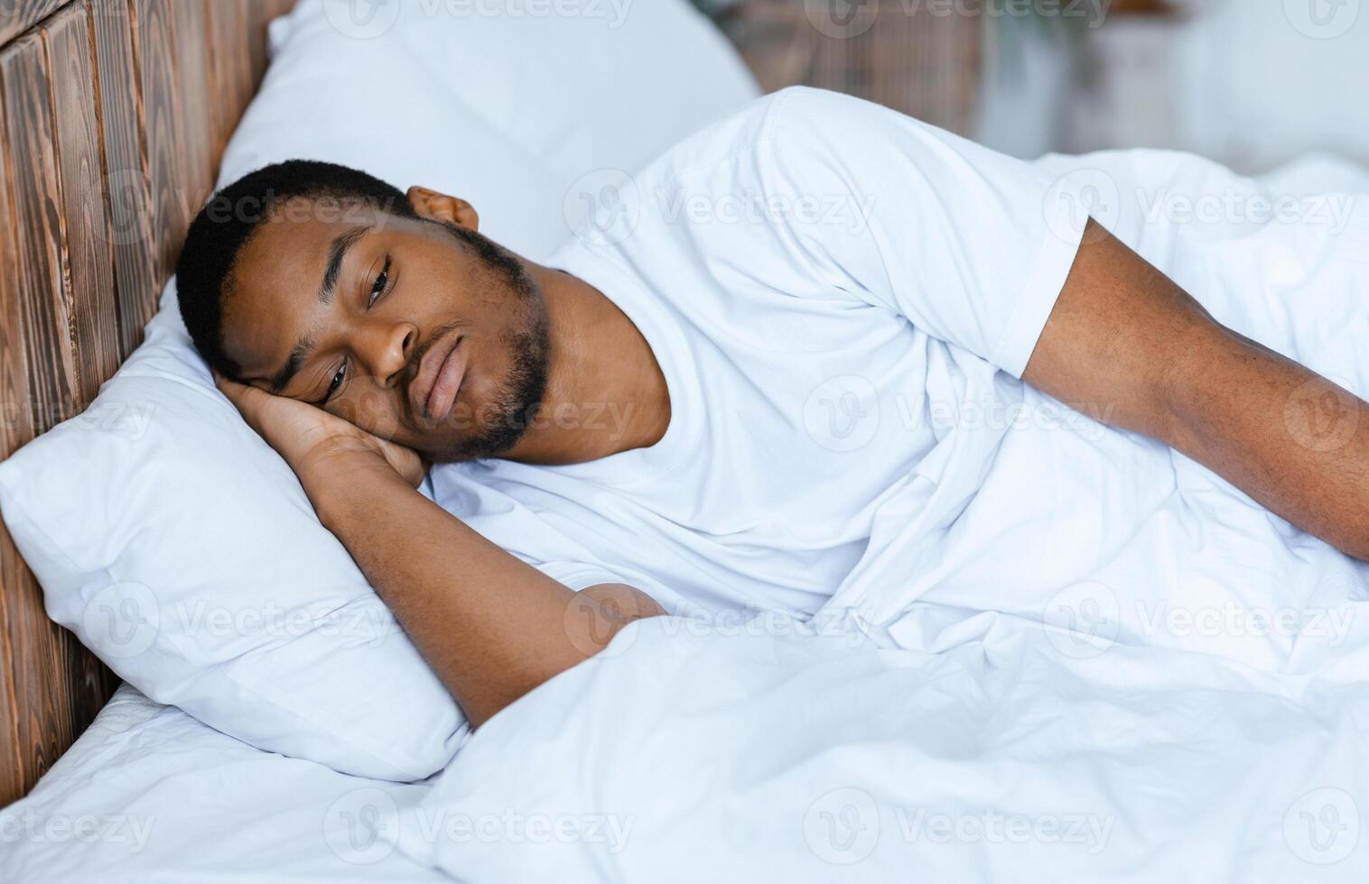 Male Depression And Apathy. Depressed Black Guy Lying Awake Thinking Of Problems Having Insomnia In Bedroom At Home At Night. Stressful Life And Sleeplessness Concept. photo