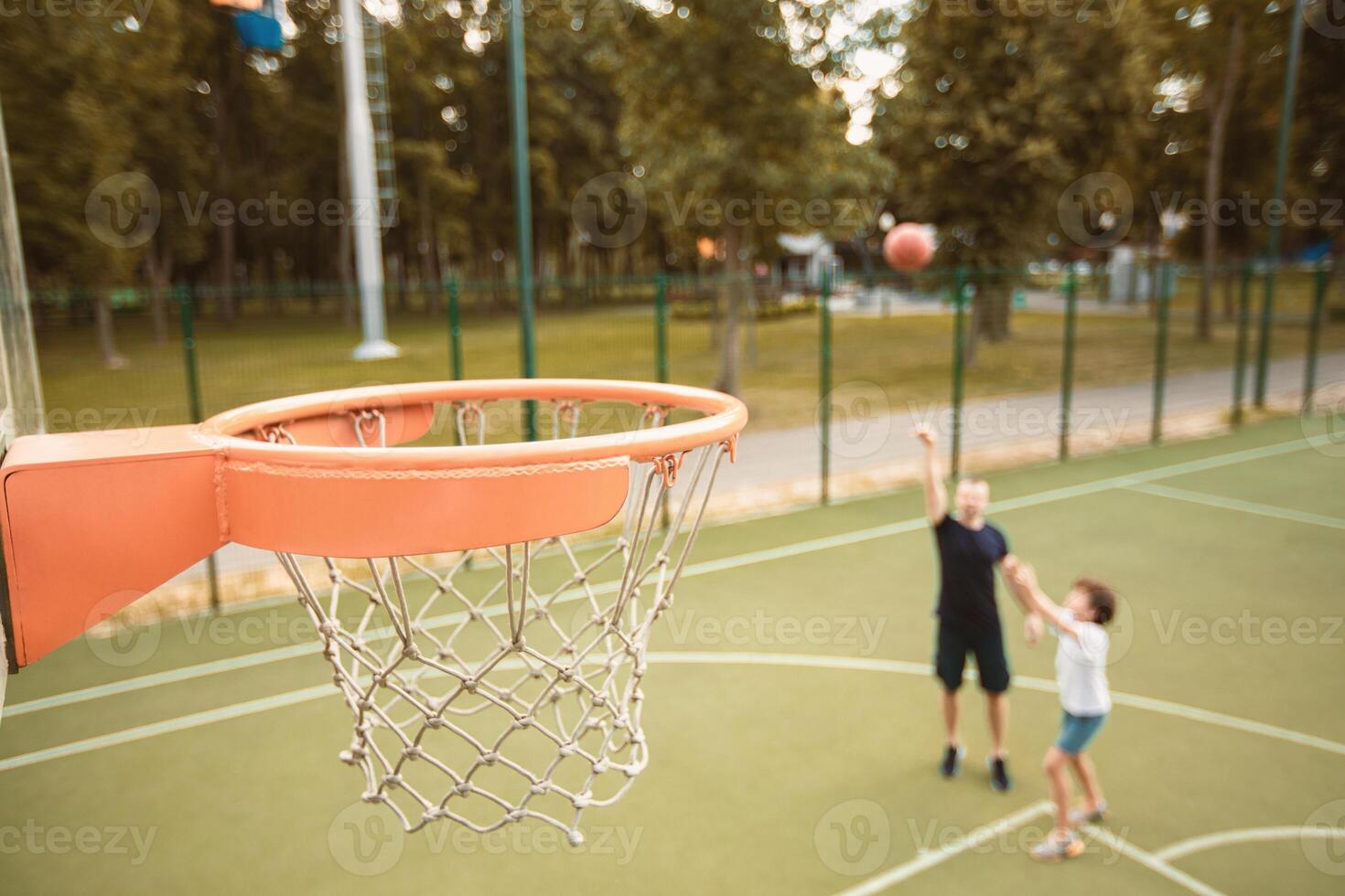Scoring Goal. Man throwing ball, playing basketball with his son, selective focus on hoop, blurred background photo