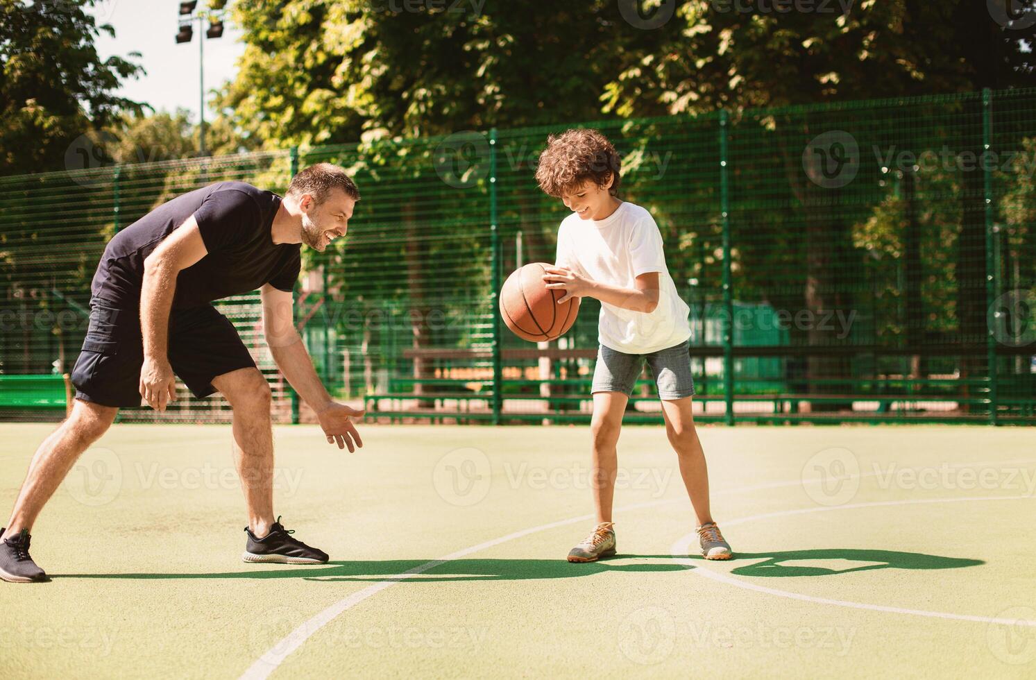 Healthy Lifestyle. Team of two players enjoying basketball game on a sports ground, kid leading the ball photo