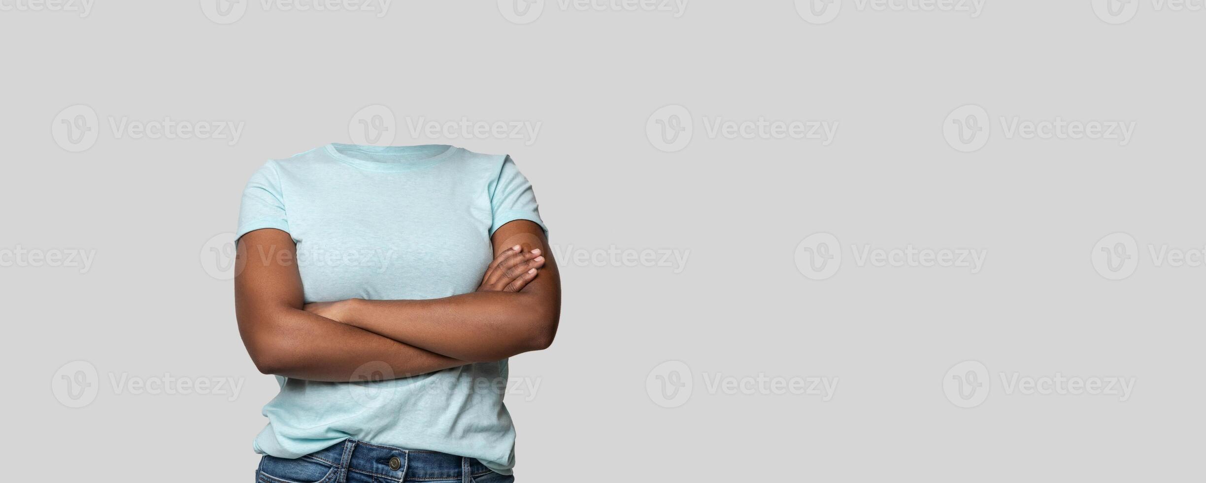 A headless person stands confidently with arms crossed, showcasing a casual blue shirt. The background is a plain, light color, creating a focused and isolated aesthetic for lifestyle portrayals. photo