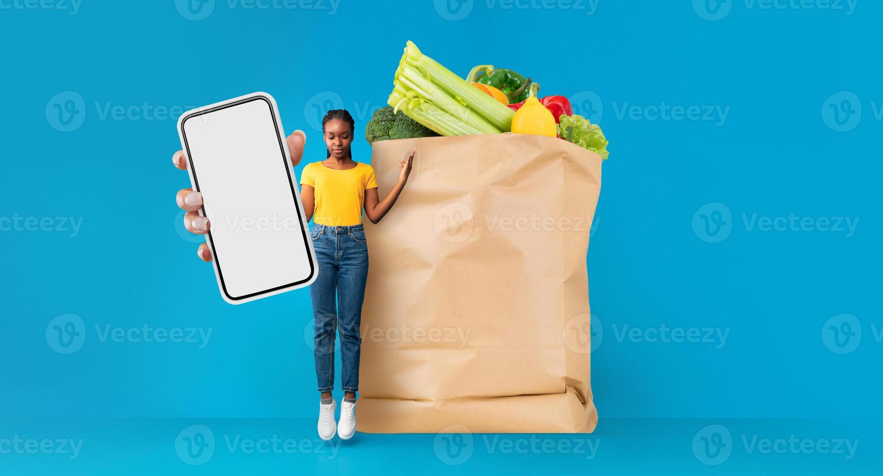 A customer stands next to a large paper bag filled with fresh groceries while holding a smartphone. This reflects modern shopping trends, emphasizing convenience and delivery services. photo