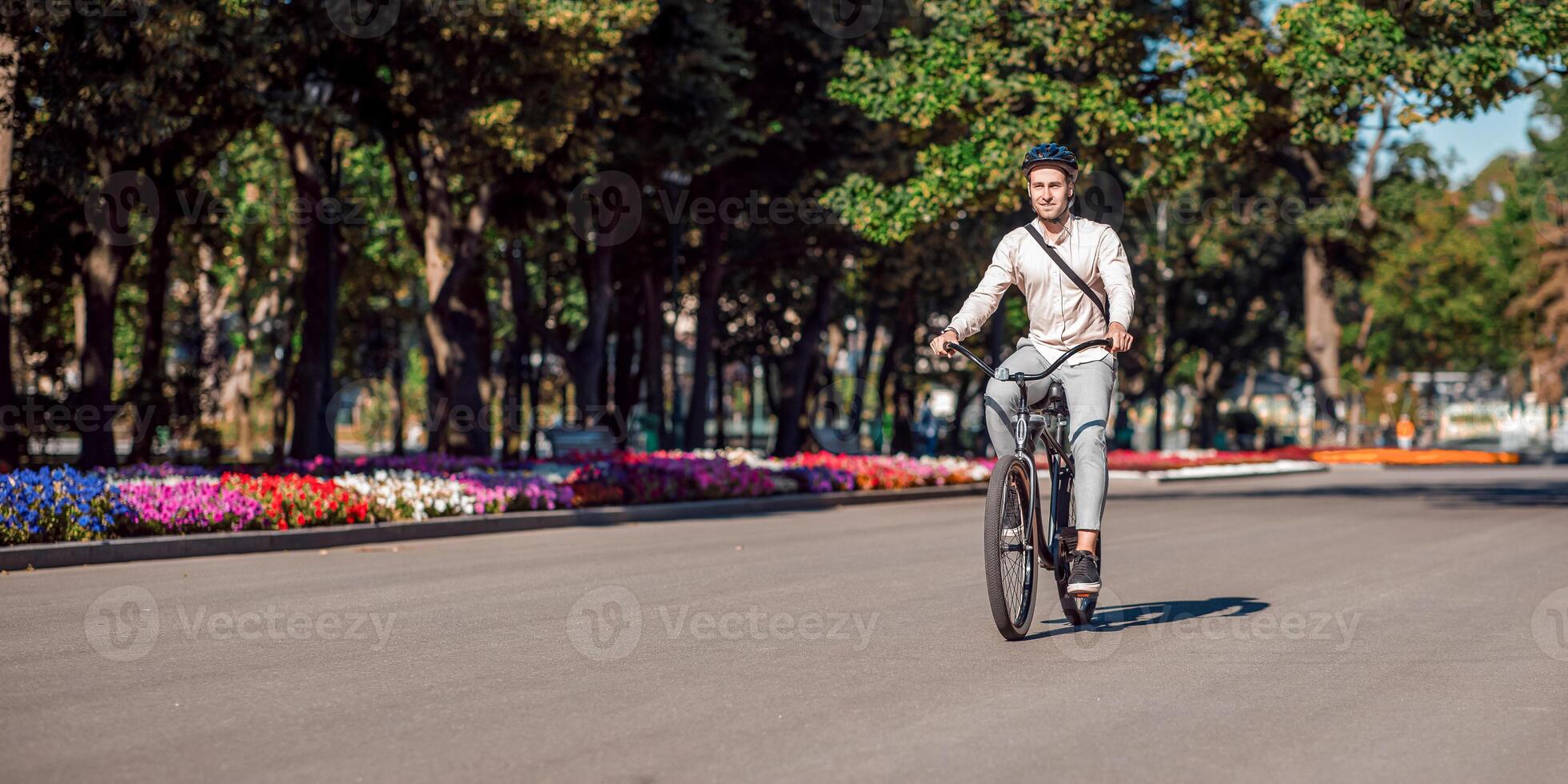 Cycling season. Man with bag on bike, smiling at camera on background of park, outdoors photo