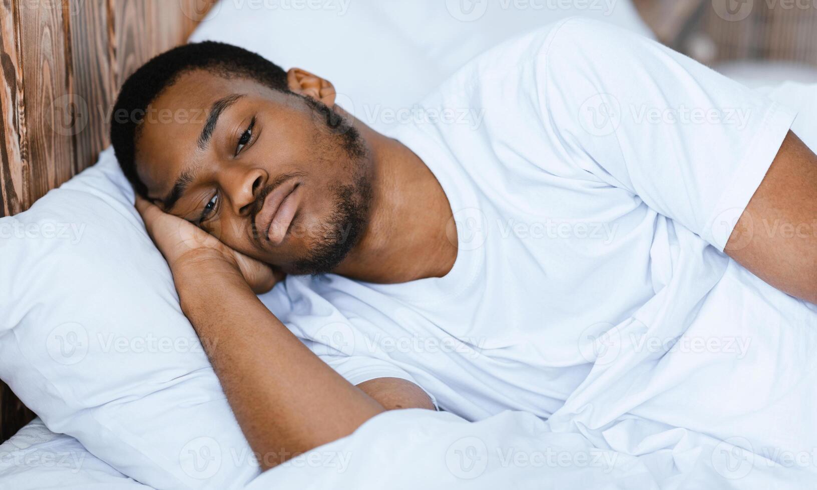 Depressed African American Guy Lying Awake In Bed Having Insomnia At Night In Bedroom At Home. Male Apathy And Depression Problem, Sleeplessness And Stress Concept. photo