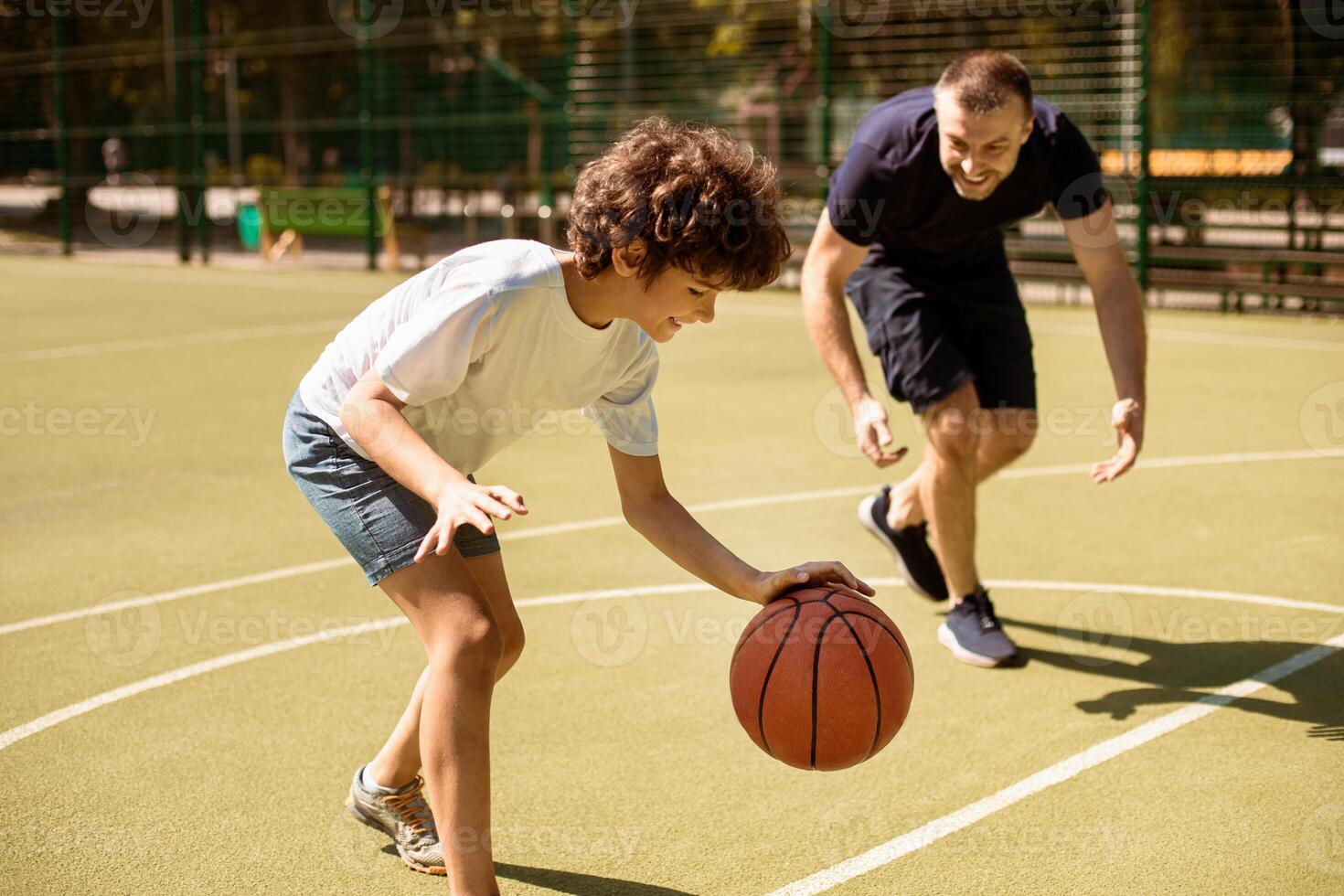 Enjoying Game. Portrait of cheerful father and son playing basketball together on a sports court, boy leading the ball and dribbling, excited man trying to take ball. Family having fun together photo