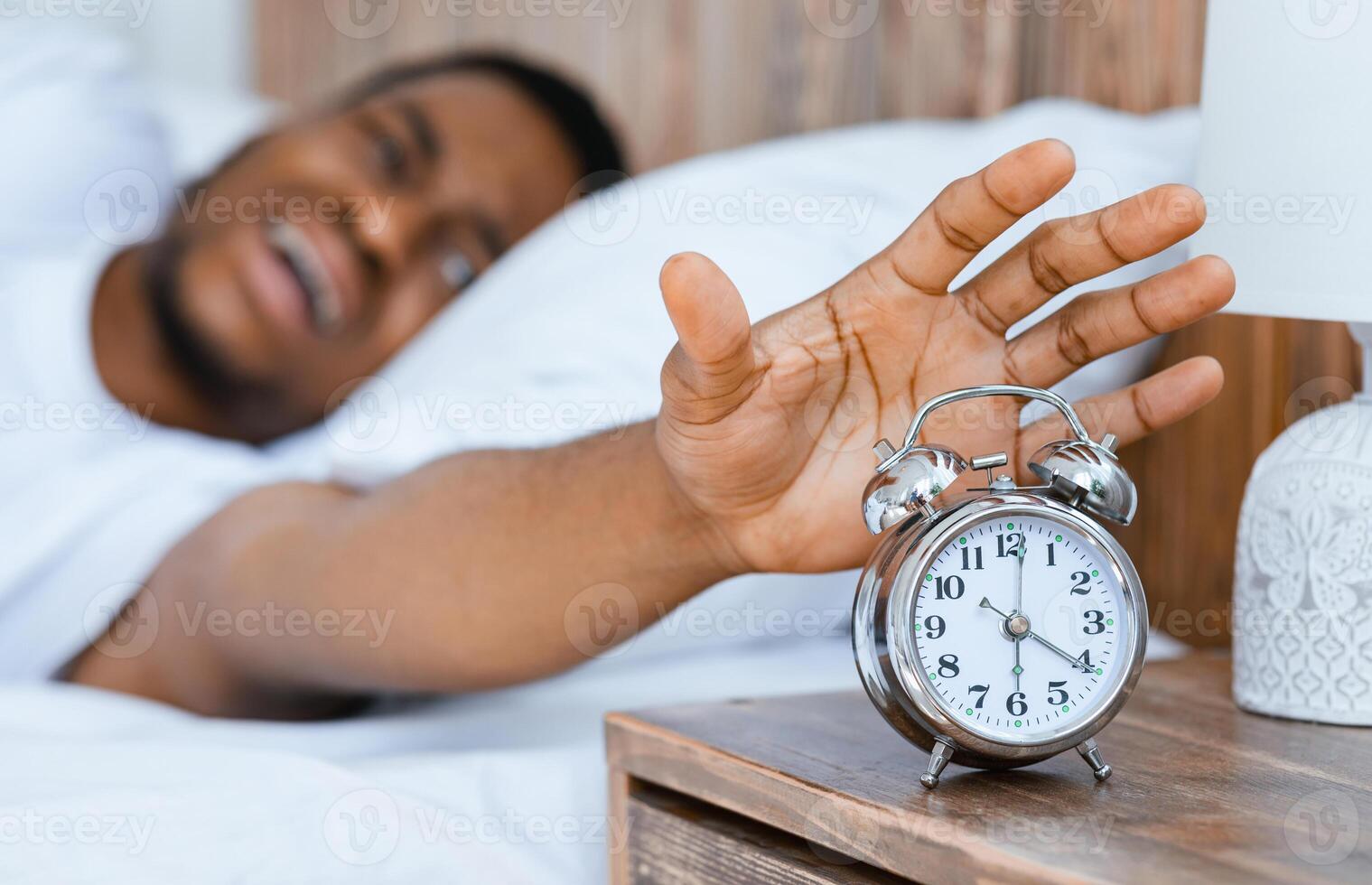 Early Awakening. Stressed African American Guy Turning Off Alarm Clock Waking Up Early In The Morning Lying In Bed At Home. Time To Wake Up Concept. Selective Focus, Shallow Depth photo