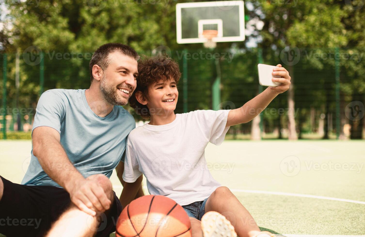 Family Selfportrait. Handsome boy taking selfie with his daddy, sitting on stadium field, blurred background photo