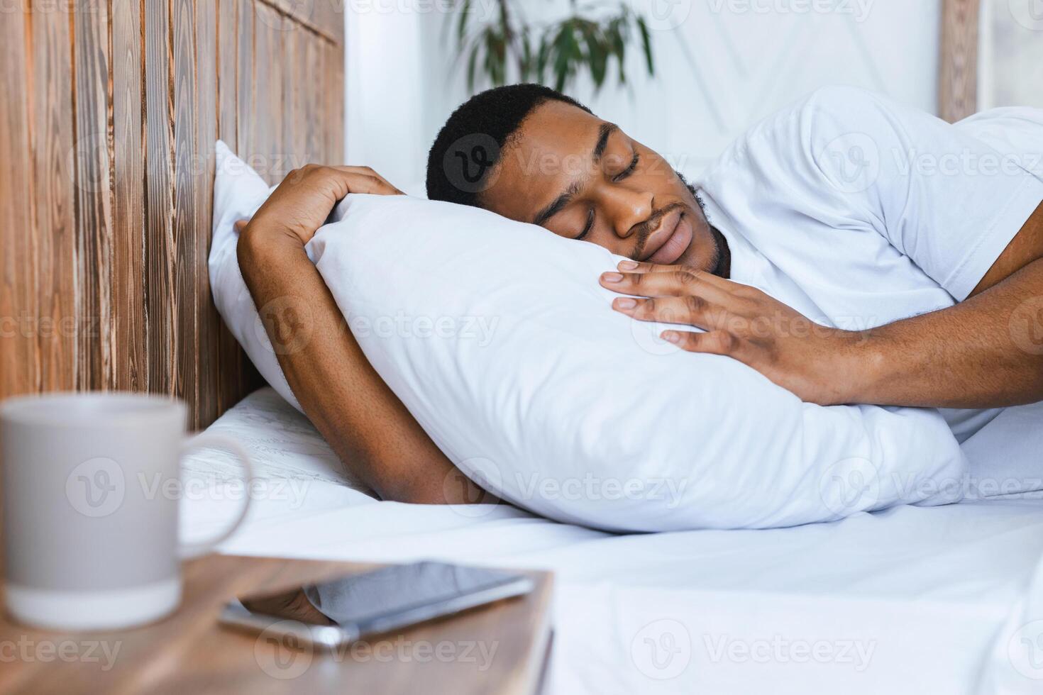 Oversleeping Concept. African American Guy Sleeping Through Alarm Clock In Morning Lying In Bed At Home, Focus On Smartphone. Rest, Nap And Recreation. Man Resting Not Hearing Alarm-Clock On Phone photo