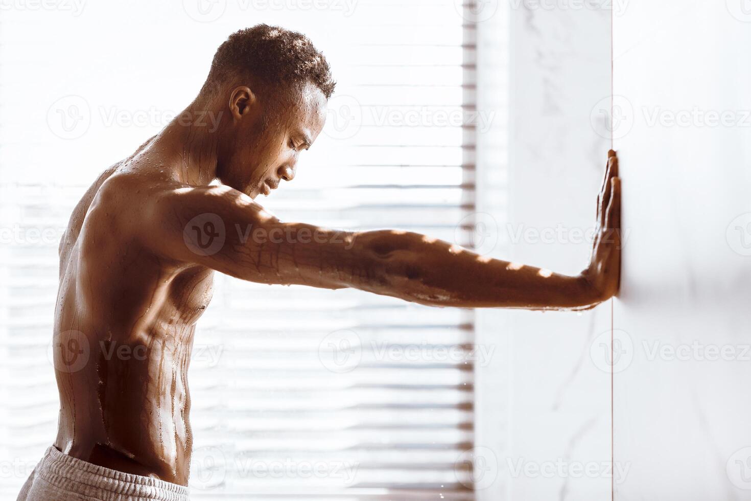 Muscular African American Man In Shower Relaxing Standing Under Falling Water Drops In Modern Bathroom Indoor, Side View. Male Bodycare And Hygiene Routine Concept photo