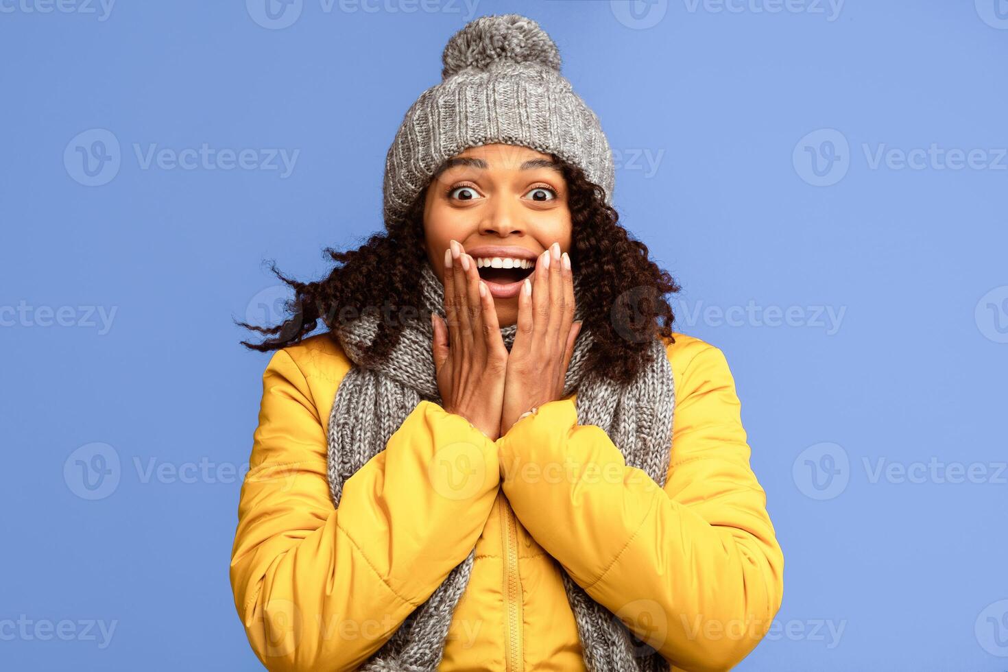 Omg. Excited African Girl In Winter Clothes Shouting In Excitement Touching Face Standing On Purple Background. Studio Shot photo