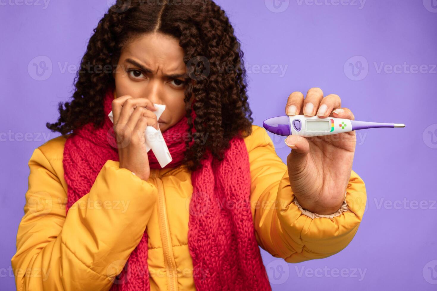 Sick Black Woman Showing Thermometer Having Fever Standing Over Blue Studio Background, Wearing Winter Clothes. Coronavirus And Covid-19, Flu Illness Symptom. Selective Focus photo
