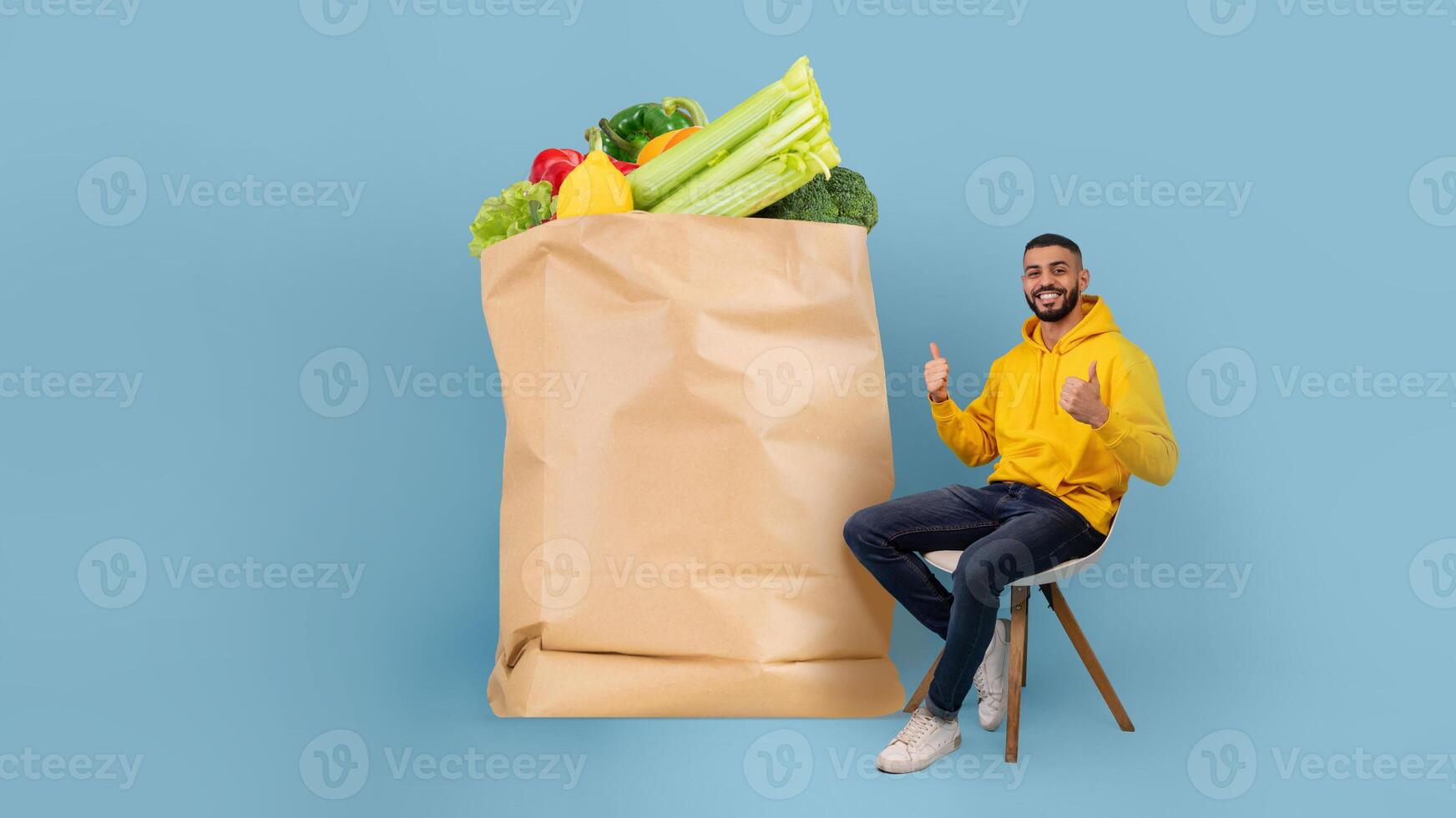 A customer sits with a large paper bag filled with fresh fruits and vegetables. The backdrop is a solid light blue, capturing the joy of online grocery shopping and delivery during current times. photo