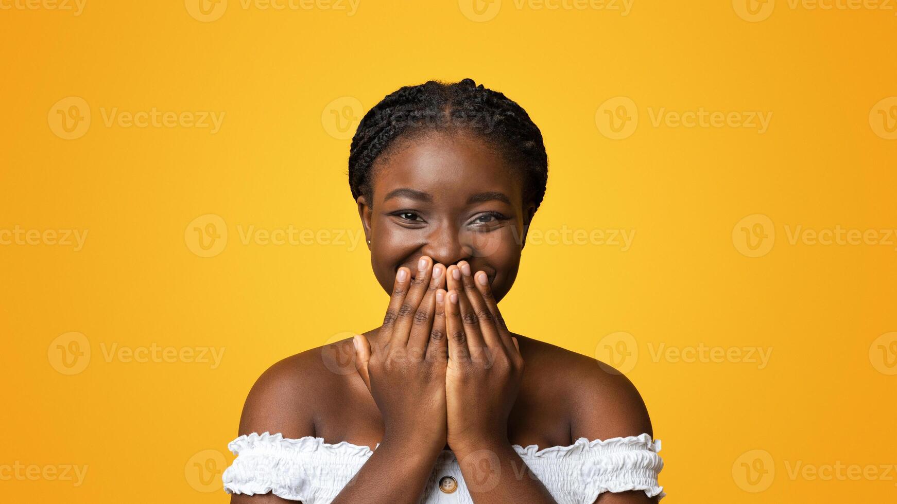 Laughter. Cheerful Black Lady Smiling And Covering Mouth With Hands In Happy Excitement, Emotionally Reacting To Pleasant Surprize, Having Positive Mood, Isolated On Yellow Background, Copy Space photo