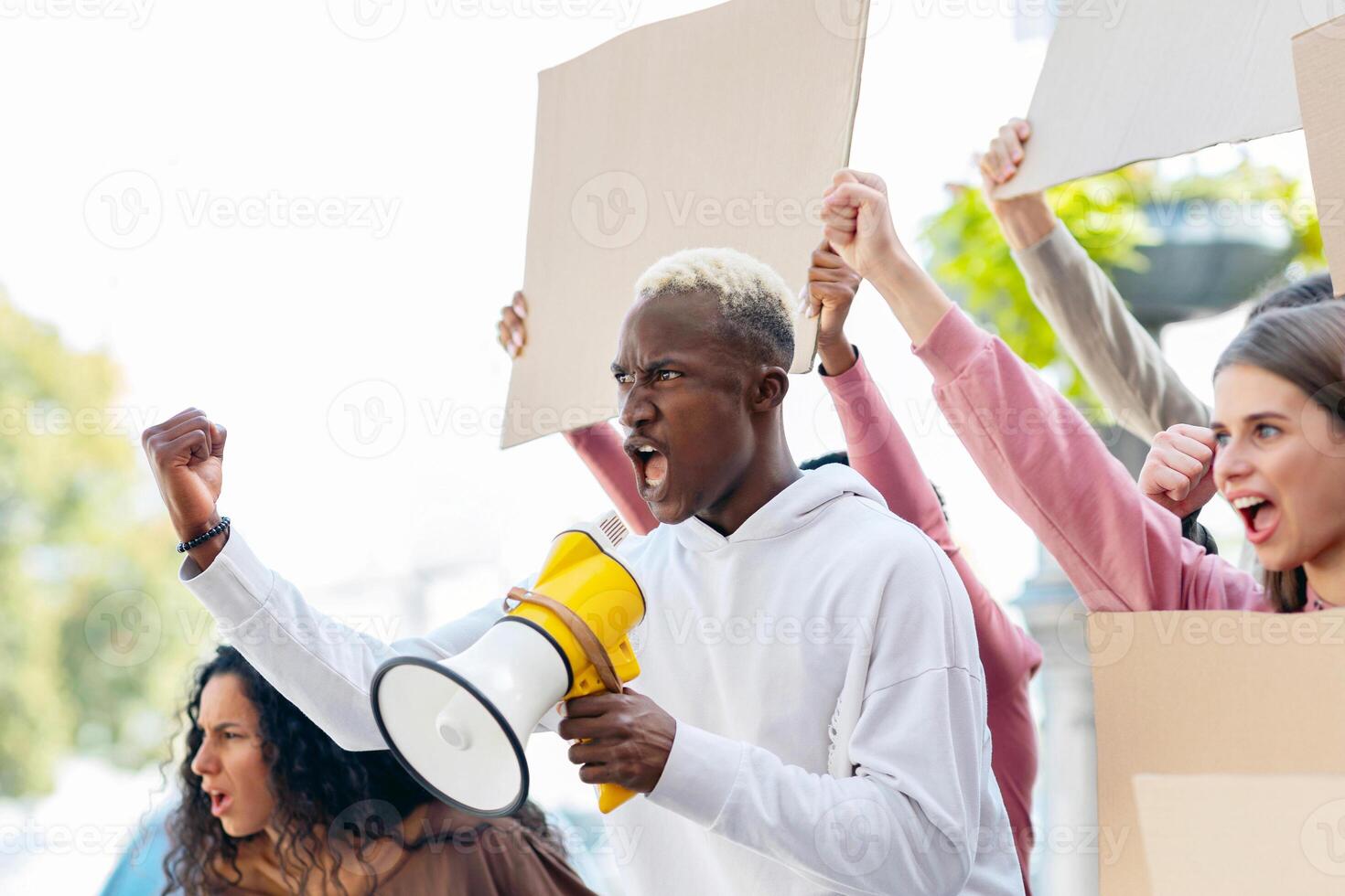 Side view of multiracial young people with blank placards chanting slogans and raising fists up, panorama with copy space. International group of young people students having strike on the street photo
