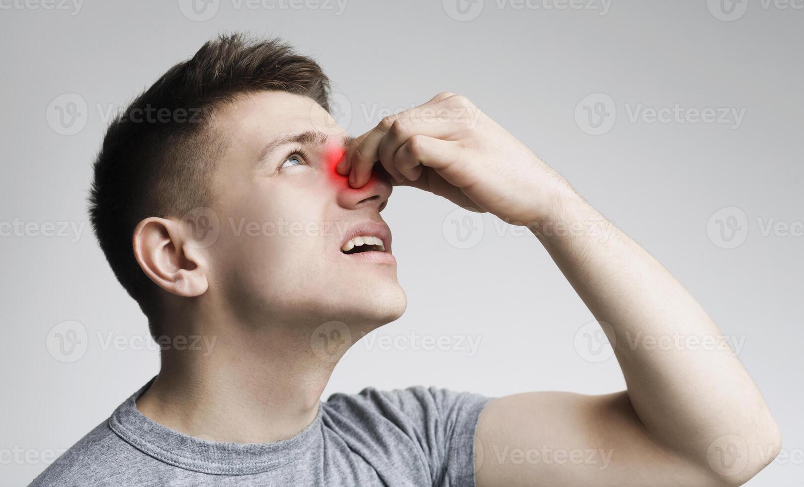 Epistaxis. Young man touching his bleeding nose, panorama, close up photo
