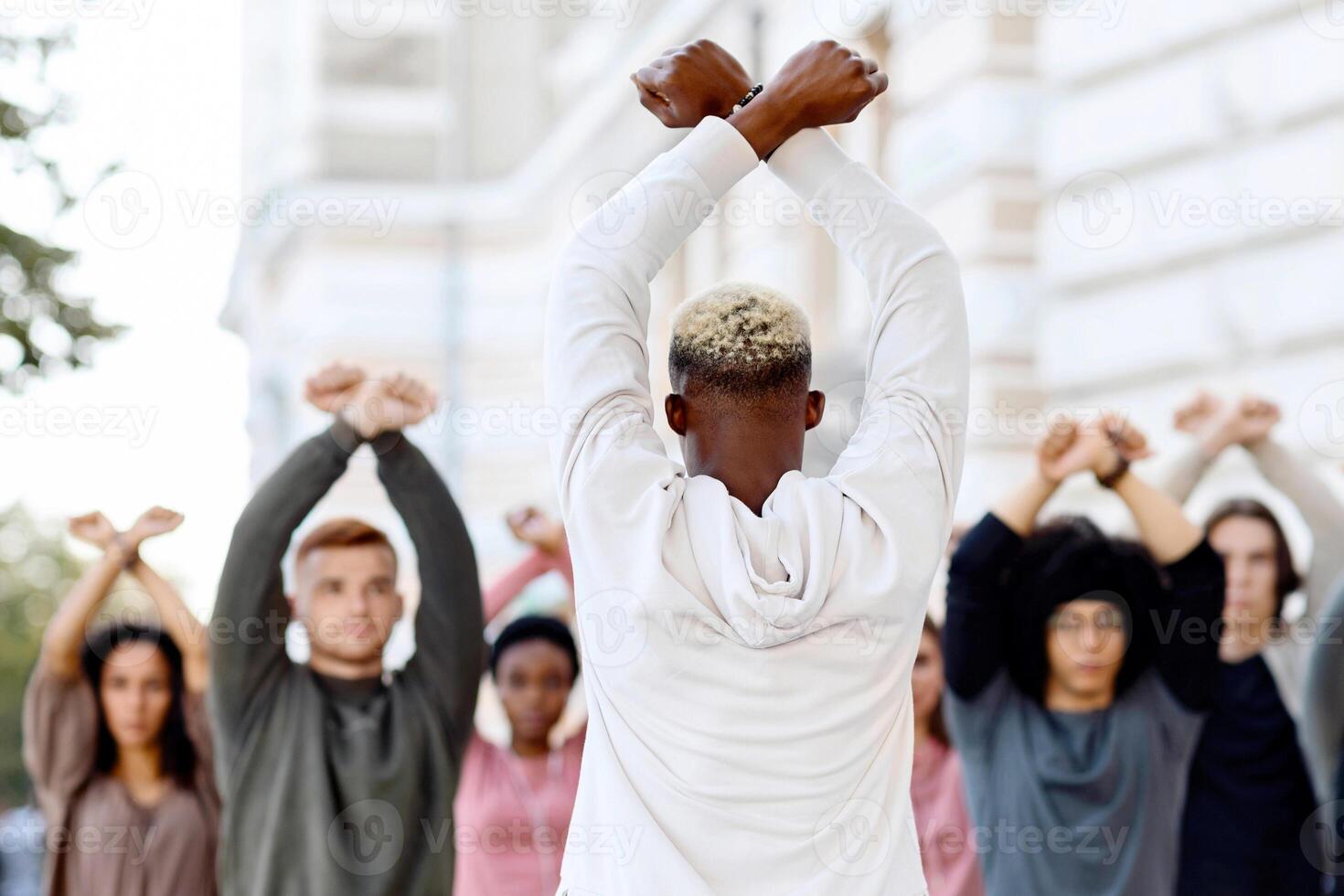 Unrecognizable african american guy leading group of protestors striking for human rights, back view of black man standing in front of multiracial strikers raising fists up and crossing hands photo