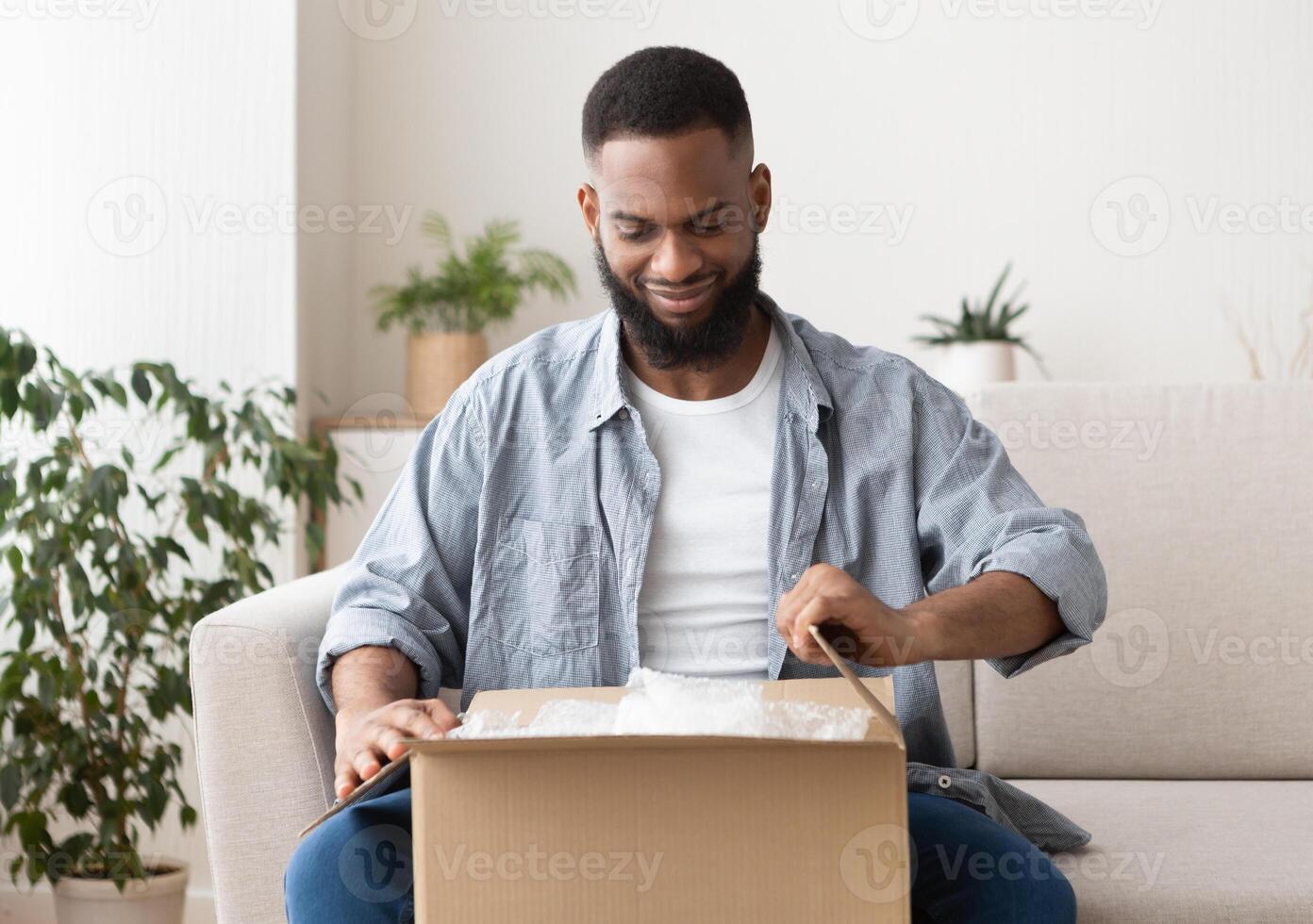 Shopaholic on the couch. African american guy unpacks purchase photo