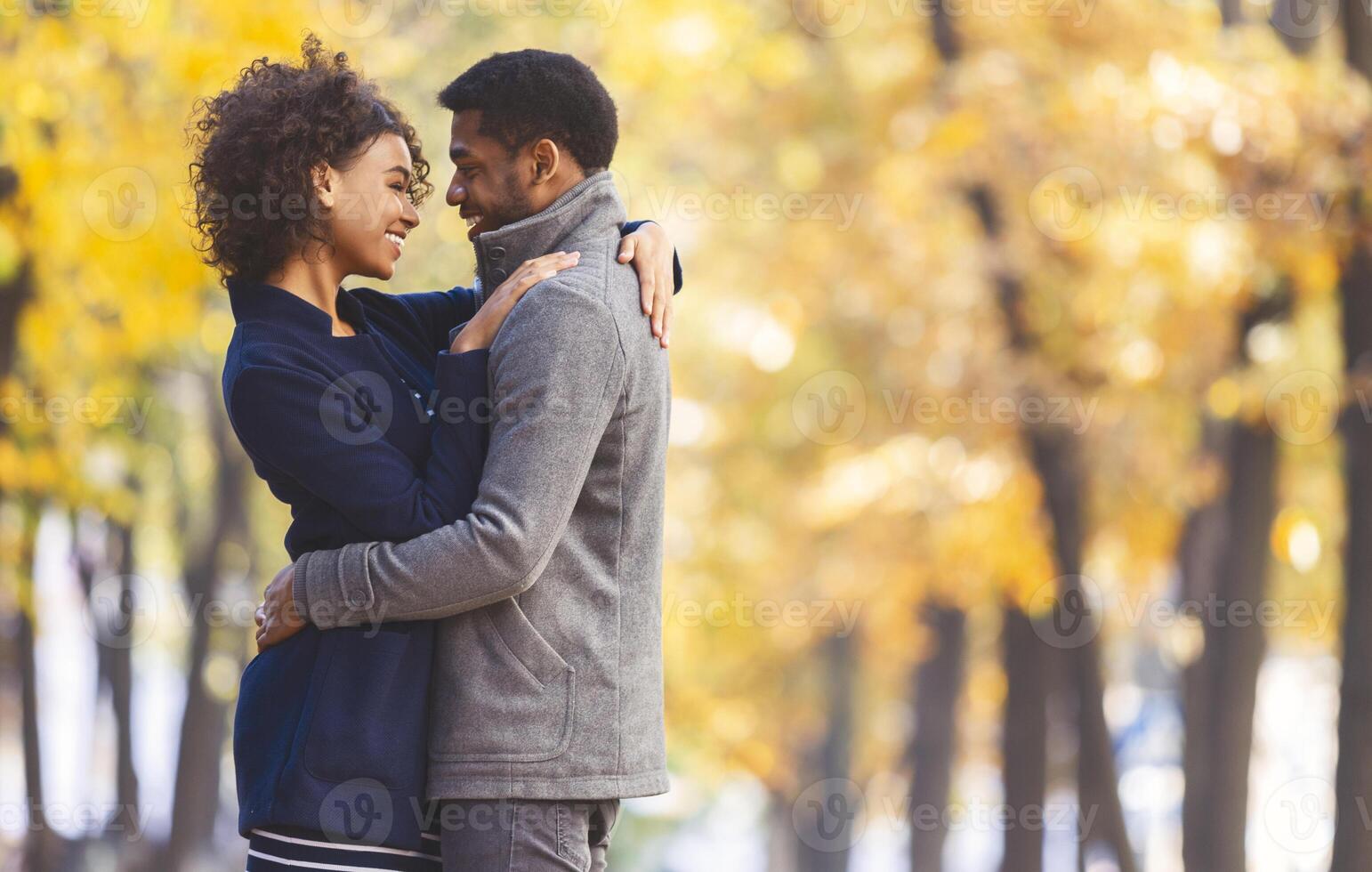 Love and romance concept. Sweet black couple hugging and looking at each other, autumn trees background, panorama with copy space photo