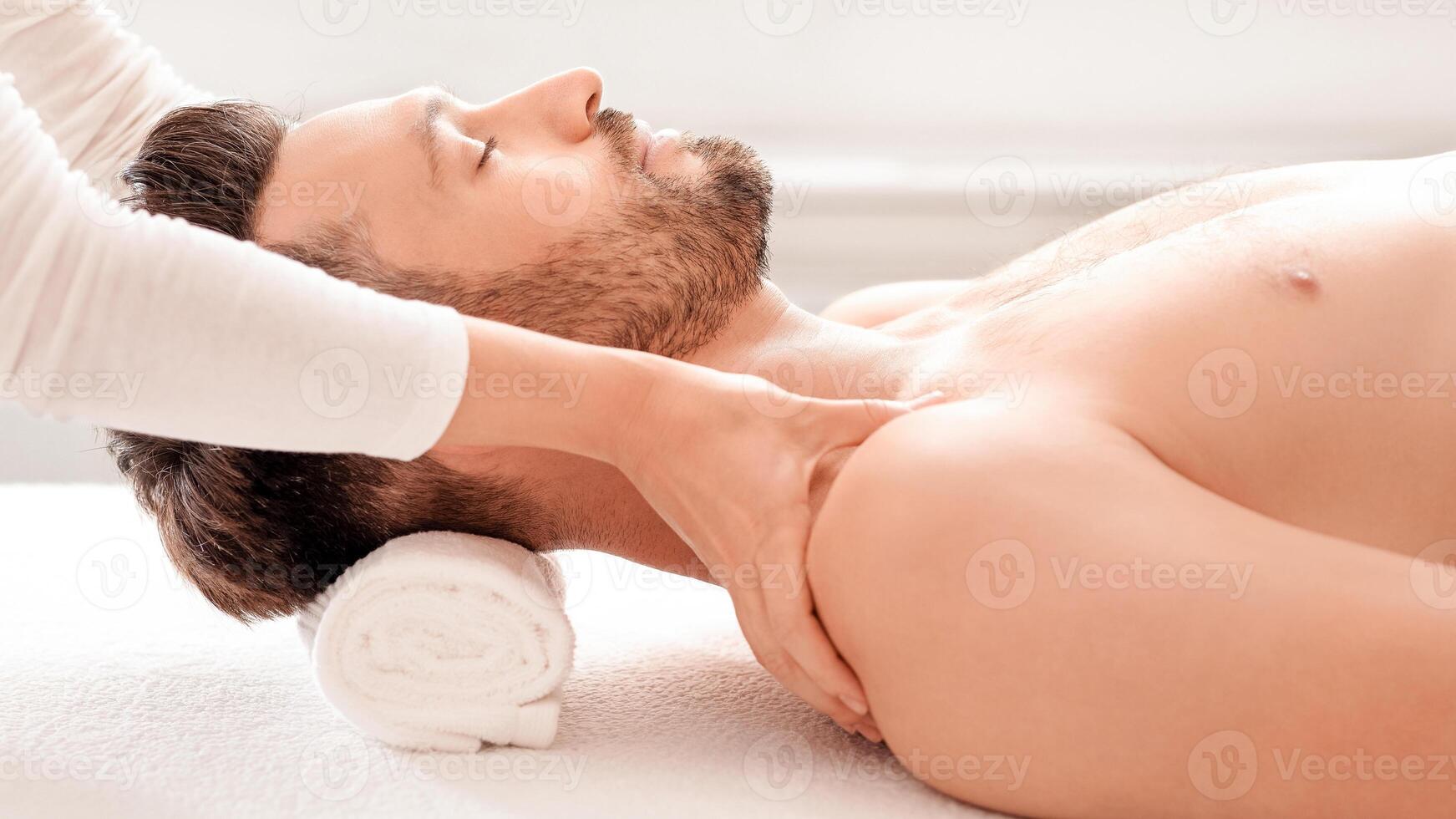Side view of relaxed handsome man getting body massage at spa salon. Middle aged bearded man attending modern male spa, laying on massage table, enjoying healing body procedure, day at spa concept photo