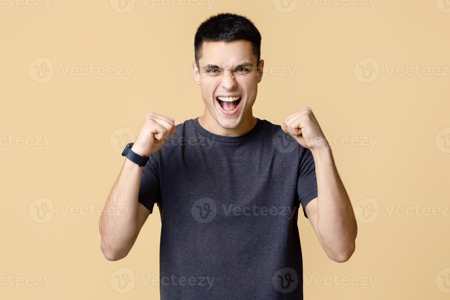 Success, victory and luck in business or work. Joyful young man with smart watch looks at camera and expresses emotions of win and success, isolated on light background, empty space, studio shot photo
