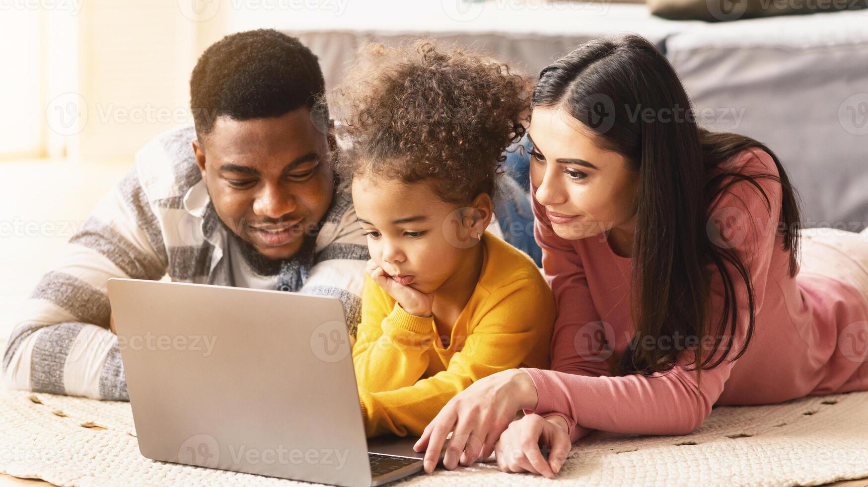 International parents teach child to use computer lying on the floor photo