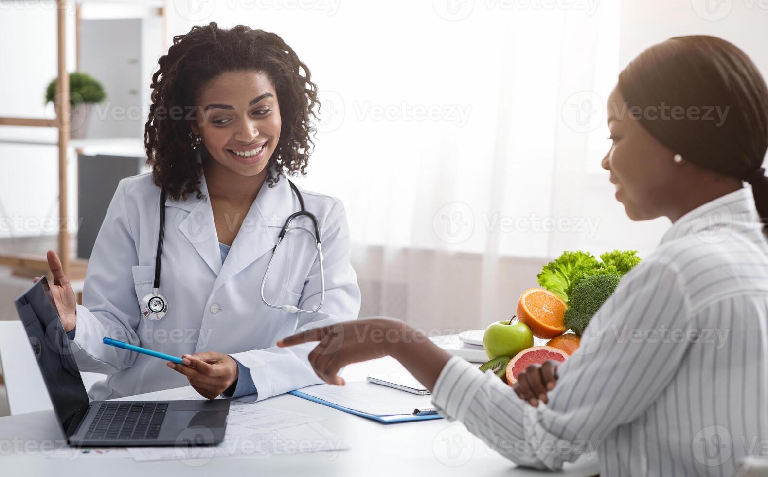 Personal nutrition plan. African american woman dietologist consulting patient, using laptop, clinic interior photo