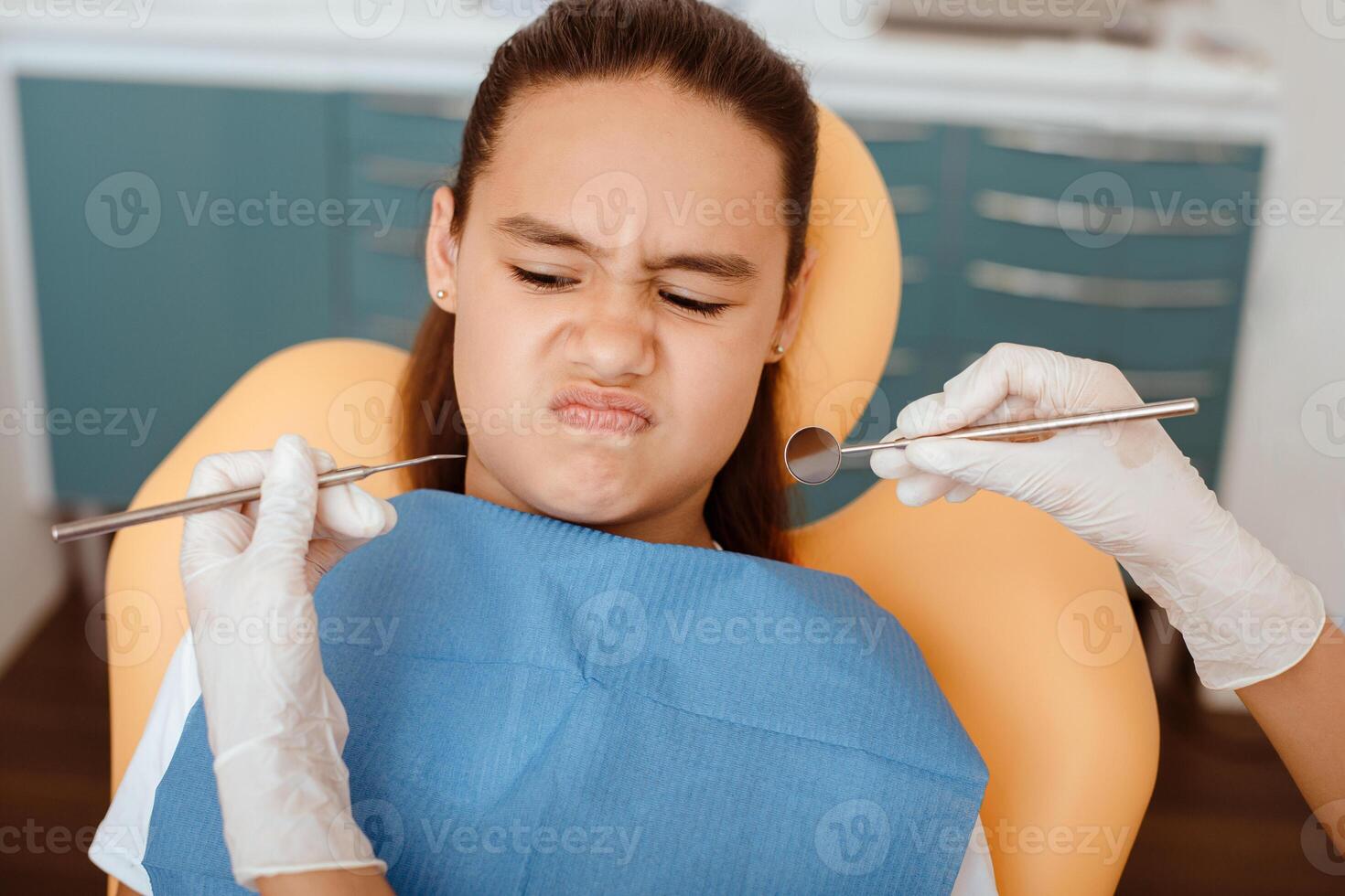 Distrust of dentist and dental treatment. Portrait of small hispanic kid in chair looking at hands of doctor in rubber gloves with medical instruments in modern clinic interior, pov, free space photo