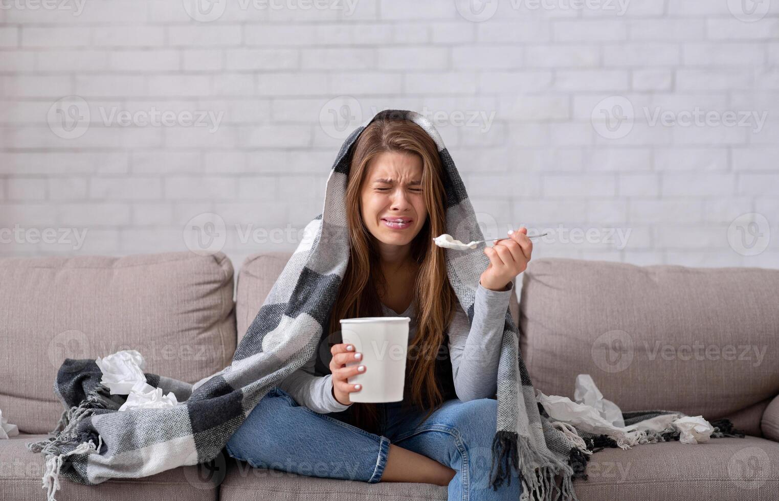 Heartbroken young woman eating ice cream from bucket while watching romantic movie on TV at home. Sad lady crying over breakup or relationship problems, feeling depressed and lonely photo