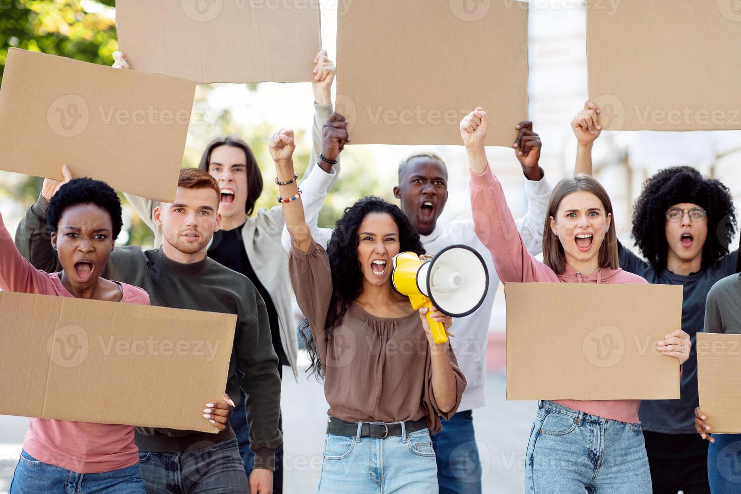 Young mixed race woman with megaphone leading a group of demonstrators with blank placards on the street. International group of people protesting for human rights, showing empty boards photo