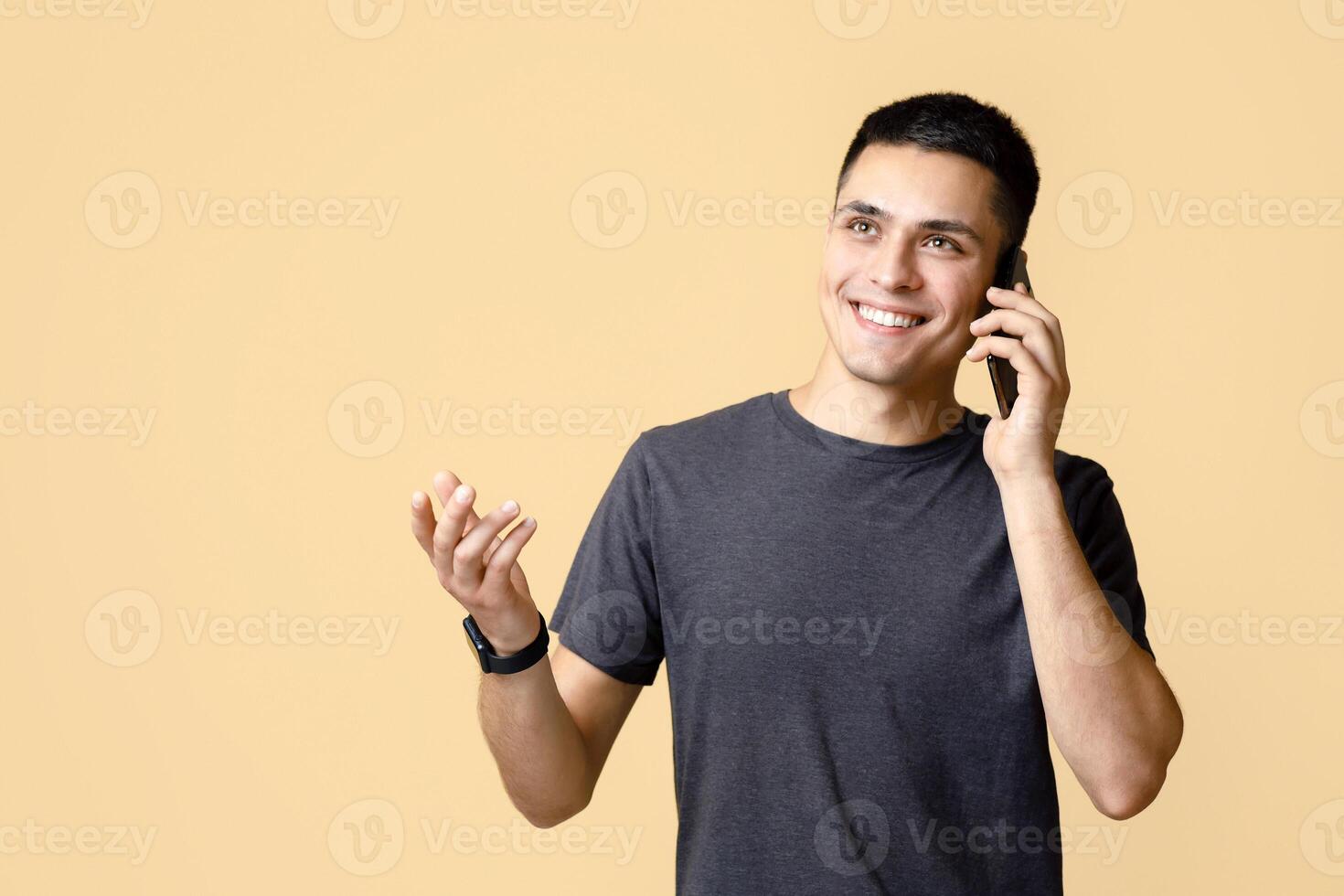 Ideas for business, modern work and communication from home. Happy cheerful young man talking on phone and gesturing, isolated on light sandy background, empty space, studio shot photo