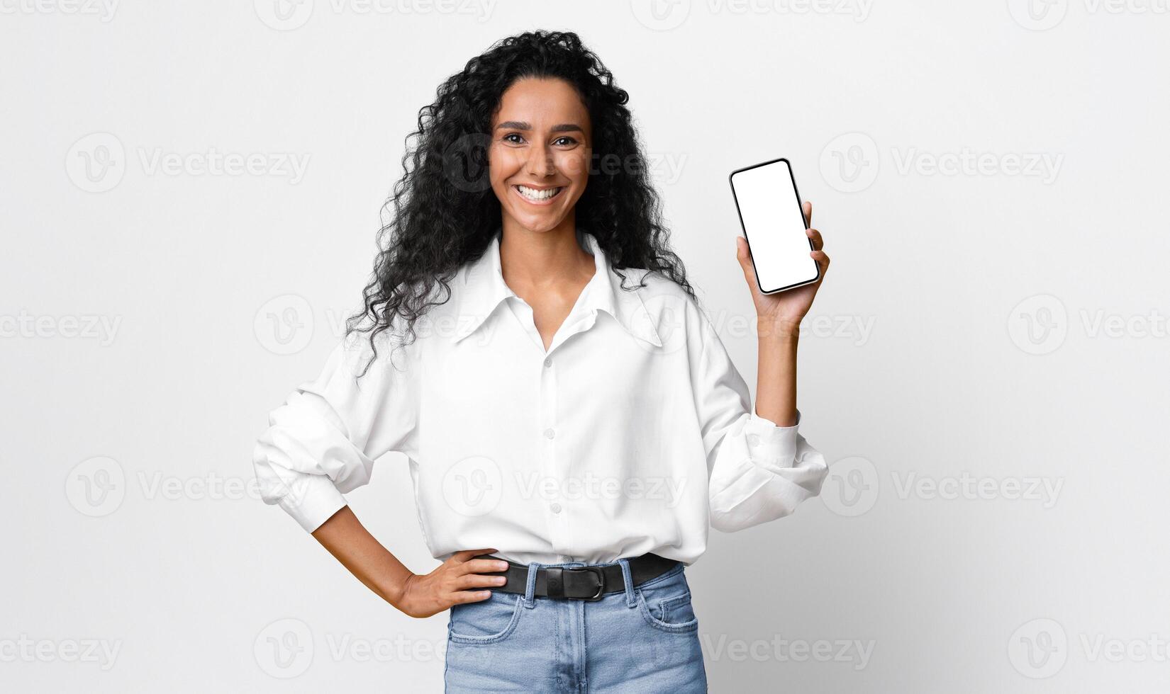Positive Millennial Lady Demonstrating Smartphone With Black Blank Screen, Showing Free Place For Your Mockup Design, Brunette Woman Recommending App Or Website, Standing On Yellow Studio Background photo