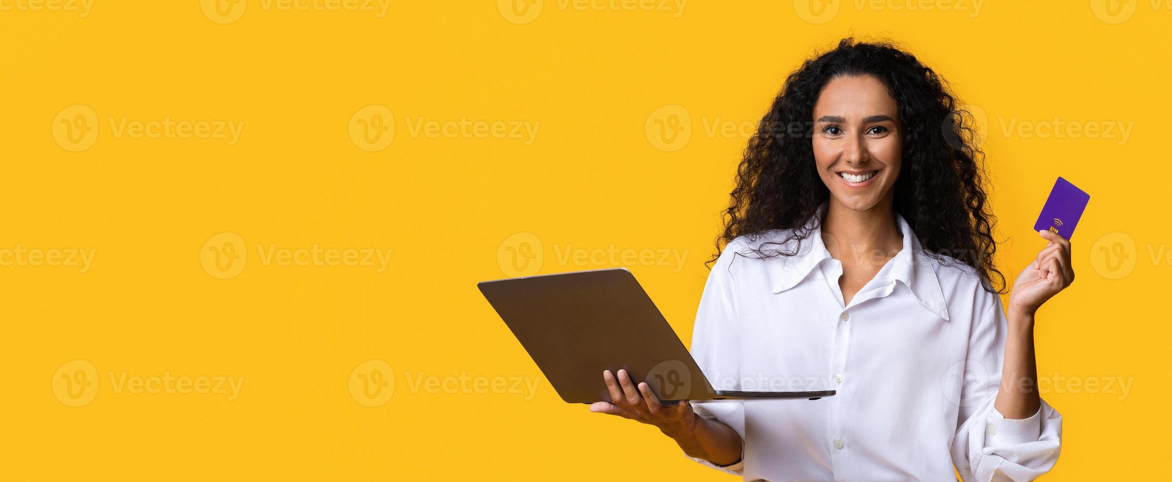Online Payments. Happy young woman with credit card and laptop, transferring money, shopping in internet, paying utilities, booking tickets for vacation, posing over yellow background, copy space photo