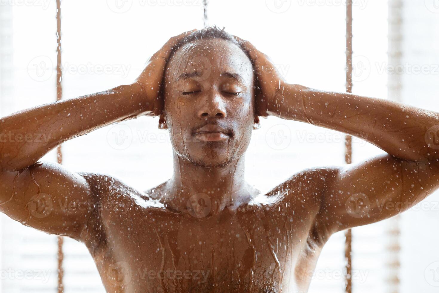 Naked Black Guy Relaxing Taking Shower, Washing Body And Head Under Falling Hot Water Stream Standing In Modern Bathroom Indoors. Male Beauty Routine, Daily Hygiene And Bodycare Concept photo