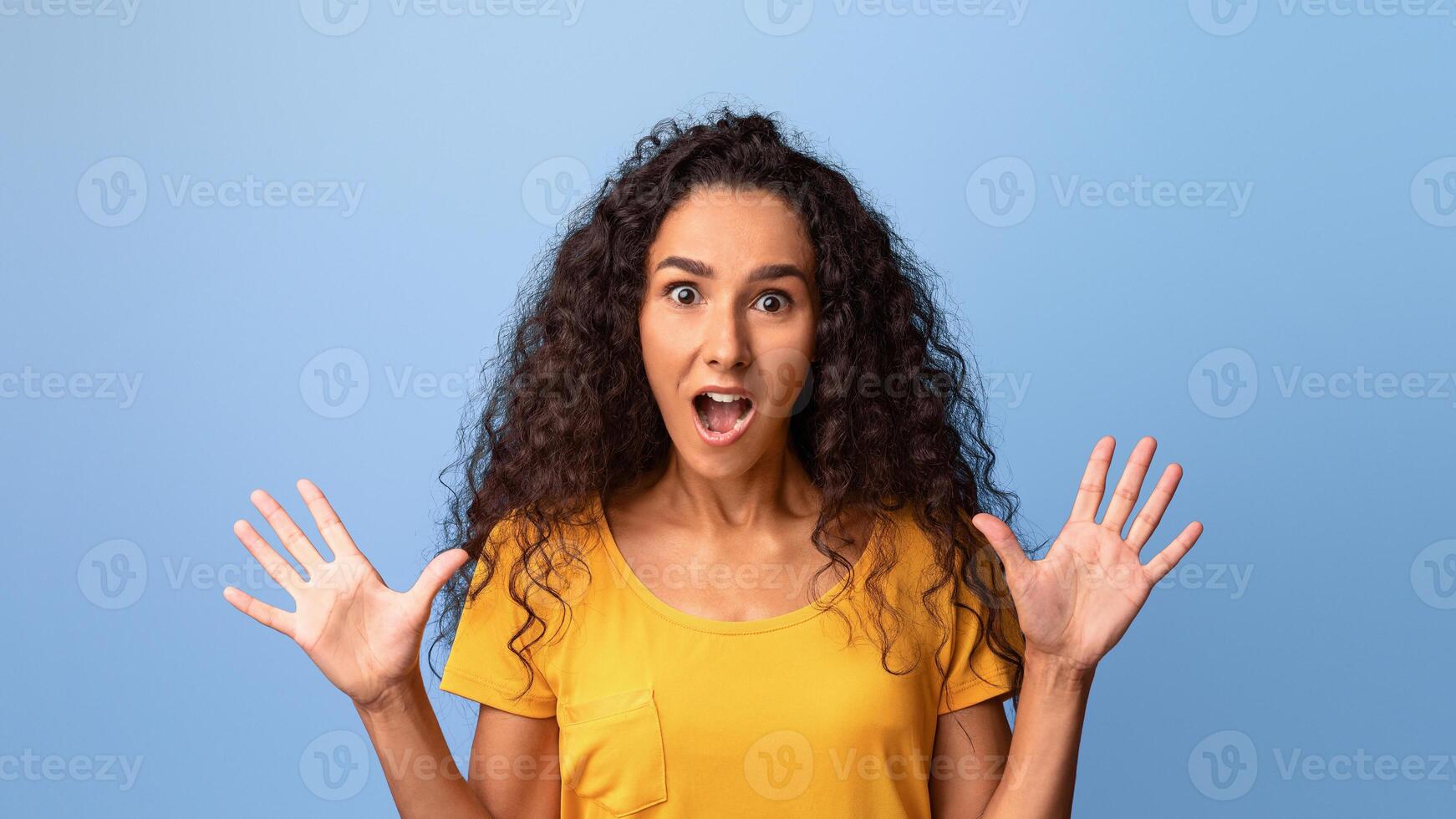 Wow. Shocked Brunette Woman Opening Mouth And Spreading Hands In Excitement, Surprised Young Lady Looking At Camera With Amazement, Posing Over Purple Studio Background, Closeup Shot With Copy Space photo