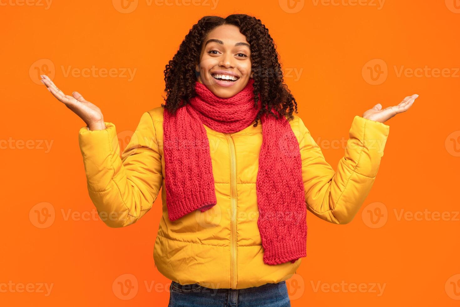 Excited Black Woman Looking At Camera In Joy Gesturing With Hands Standing Over Yellow Studio Background, Wearing Winter Jacket And Scarf. Positive People Emotions, Excitement Concept photo