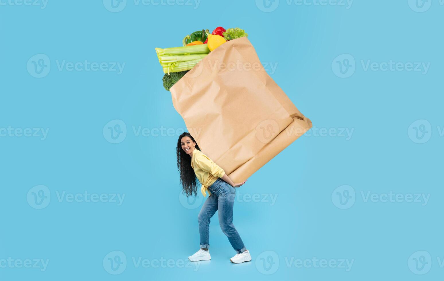 A customer joyfully carries a heavy paper bag filled with fresh vegetables and fruits in a store. This highlights the modern shopping experience amid the new normal of grocery shopping. photo