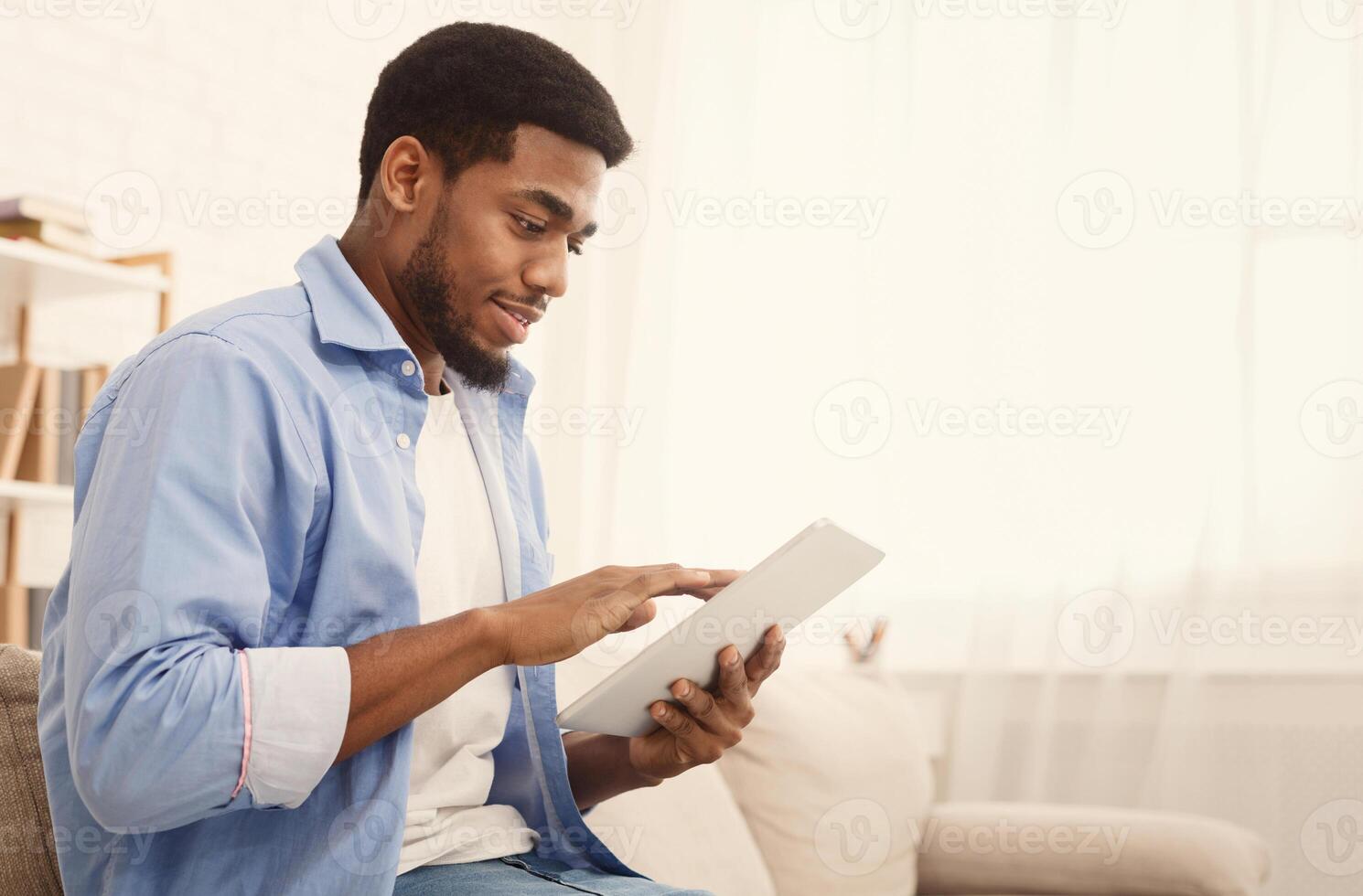 Young african-american guy using digital tablet, connecting wifi at home, empty space photo
